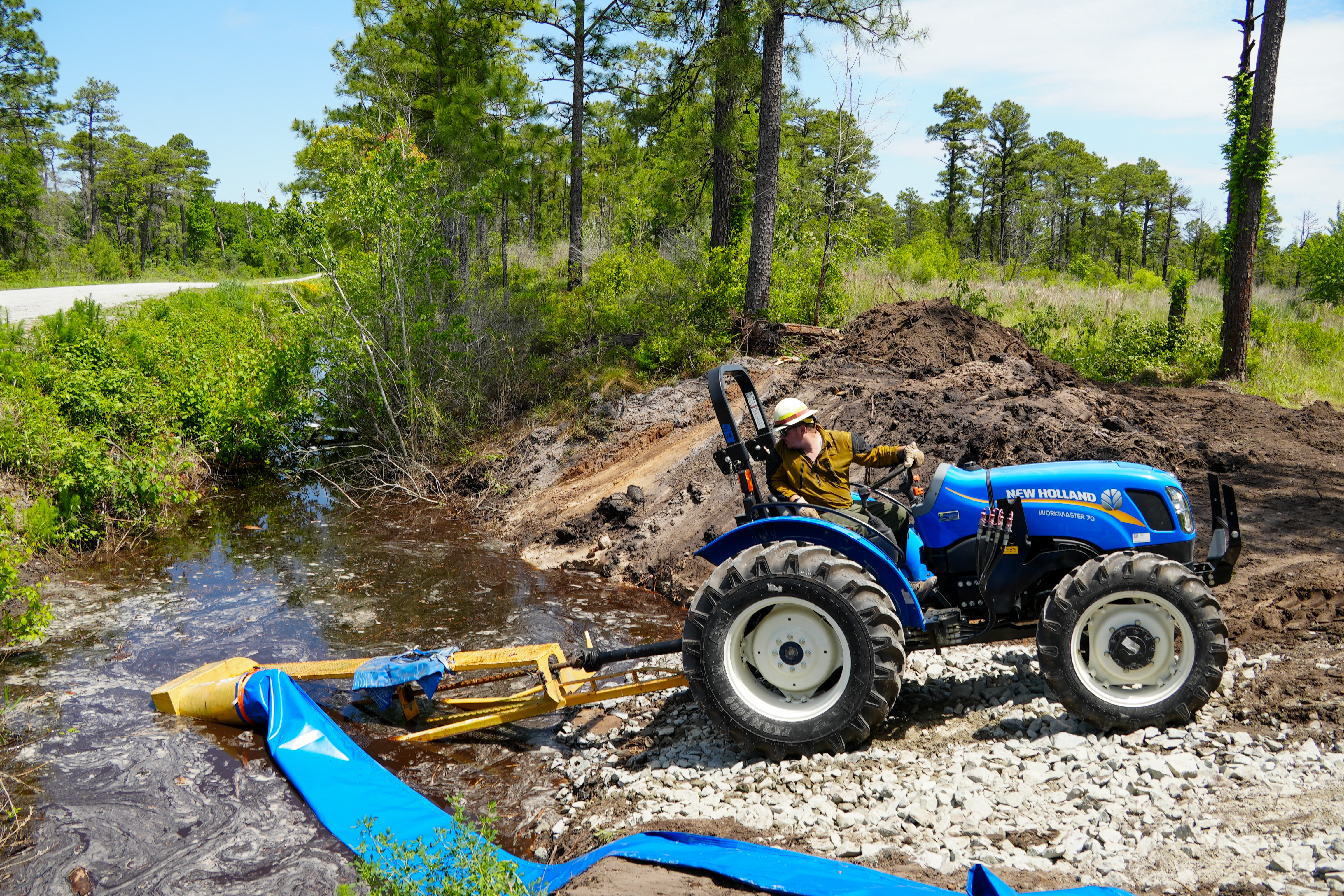 







						Tractor and pump transport water over an earthen dam
			



