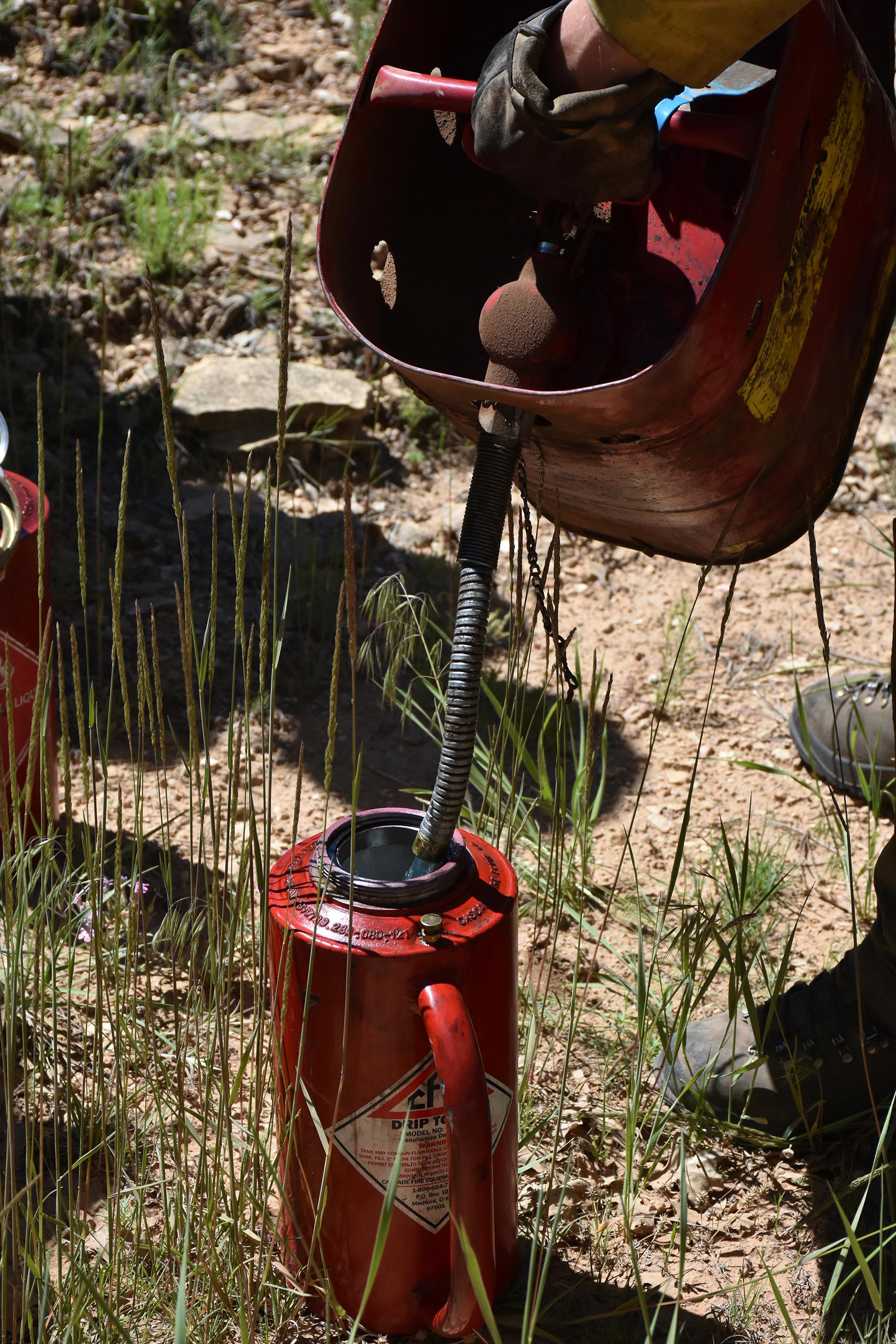 Refueling the drip torch so the firefighter can drop fire.