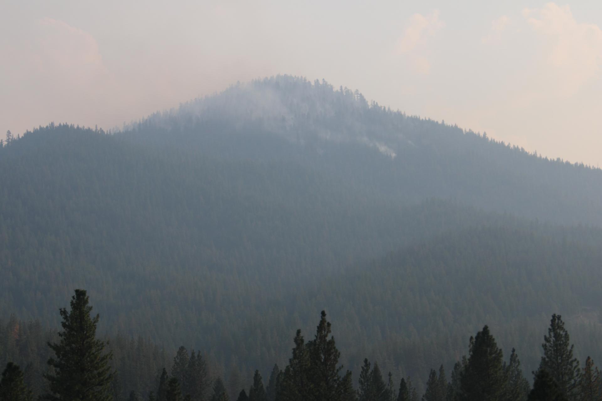 Smoke in and above a heavily forested mountain.