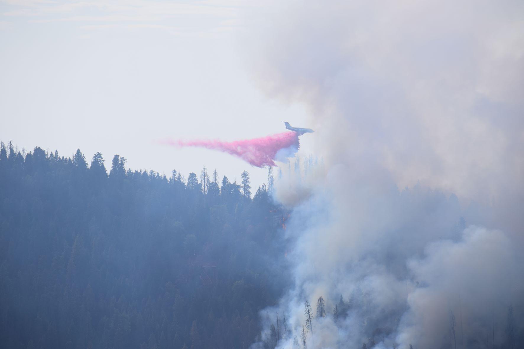 Aircraft dropping fire retardant on Colony Fire. Fire smoke and tree line visible below.