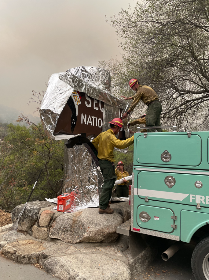 Firefighters wrap shiny material around a large wooden sign