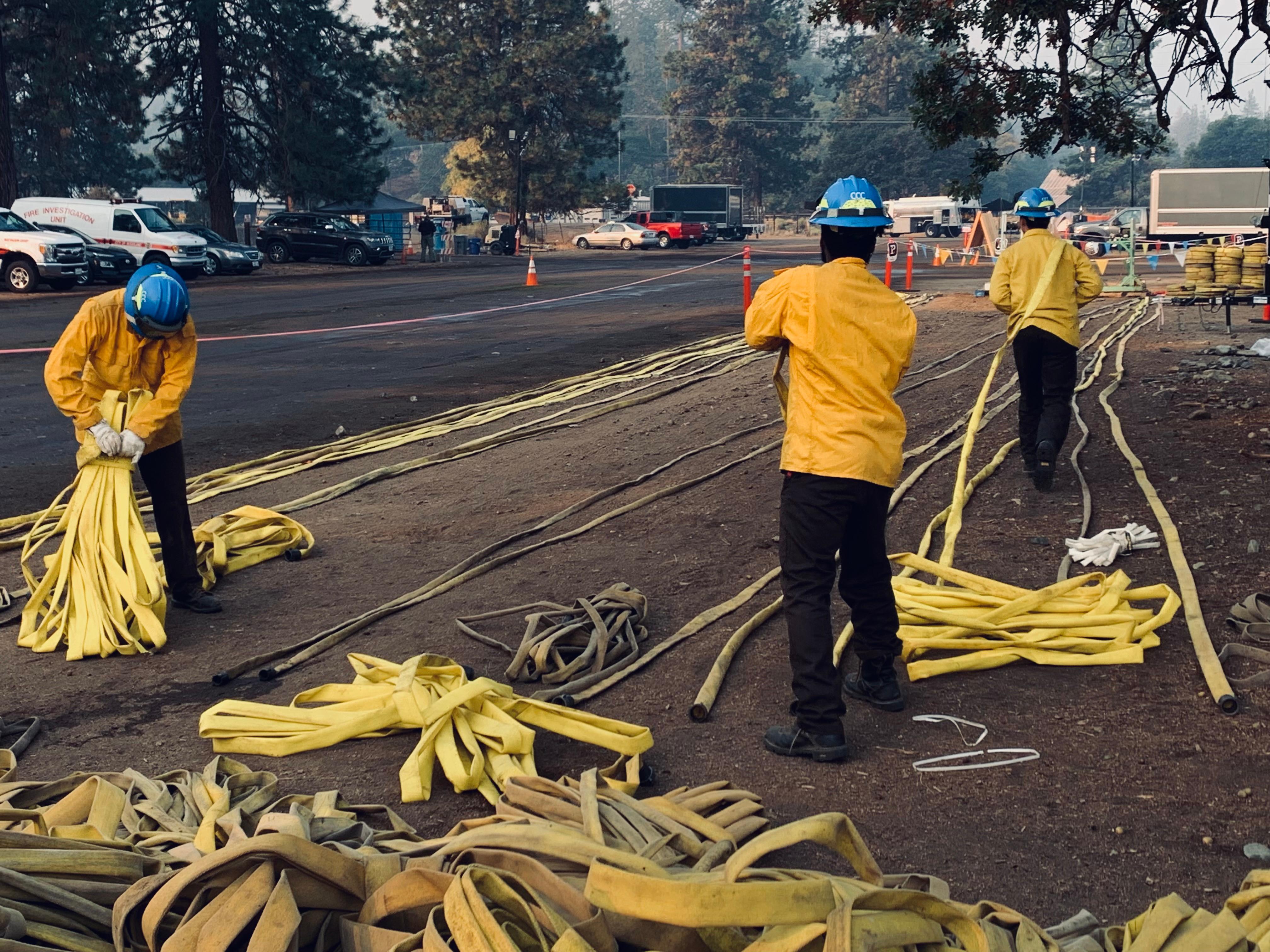 Three people organizing many hoses that are laid out on the ground