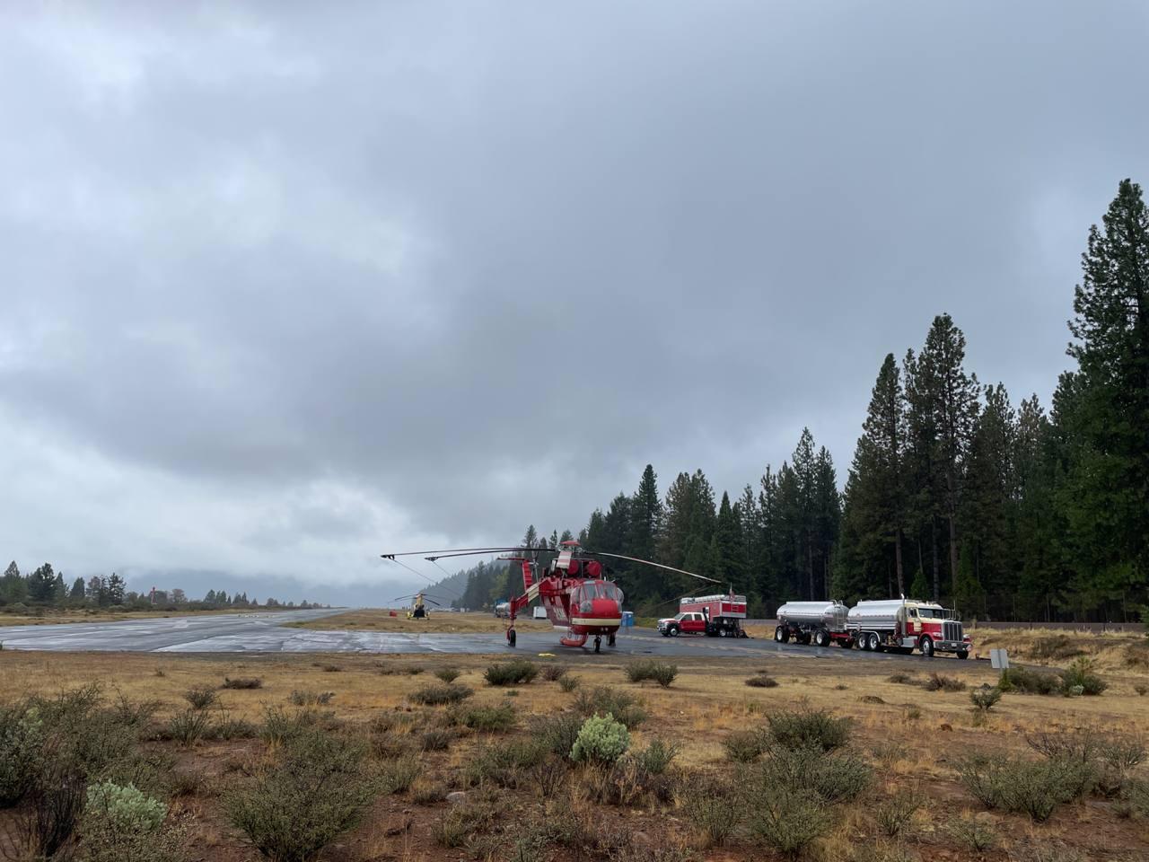 A red helicopter on the ground, a cloudy sky over head.