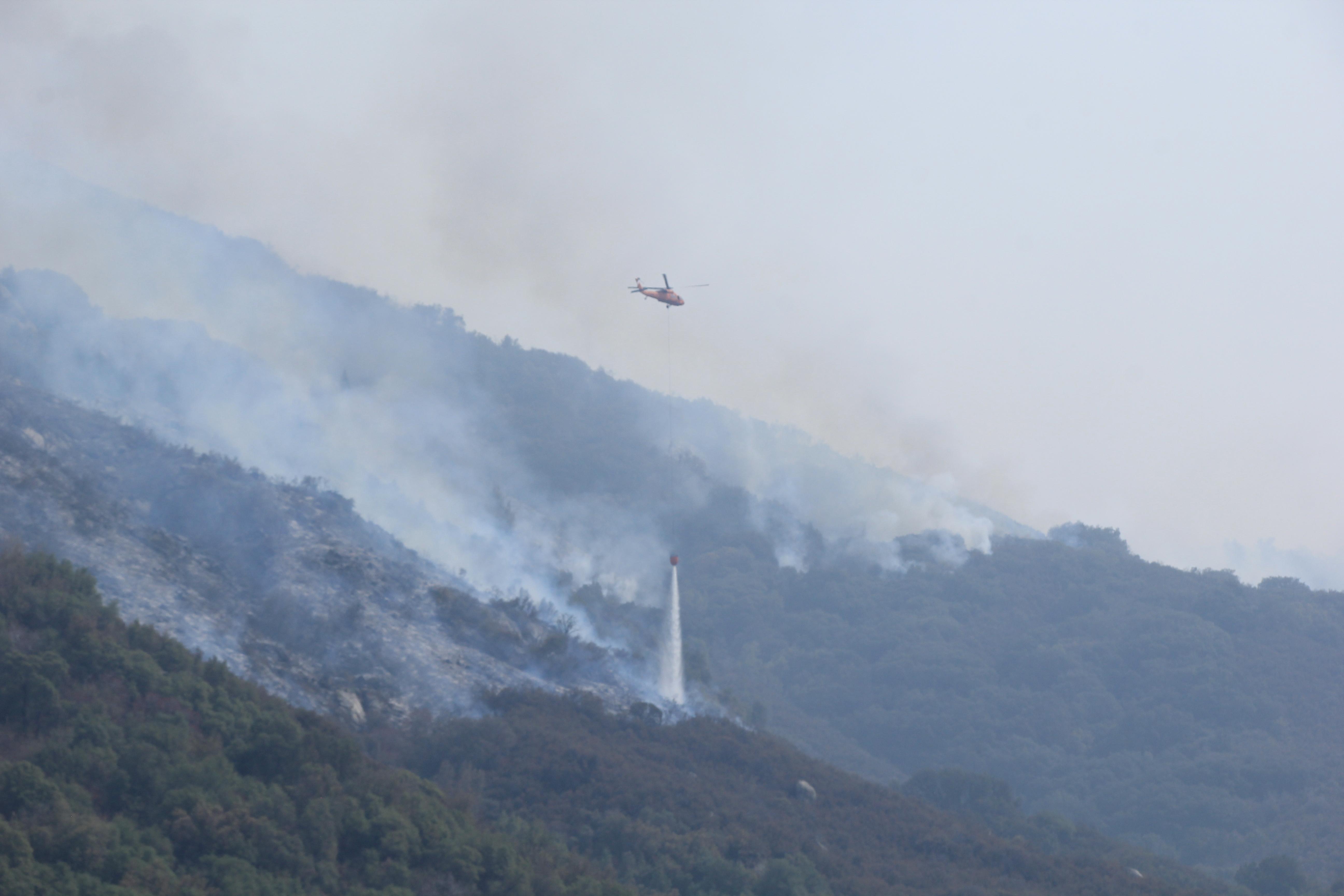 An orange Blackhawk helicopter drops water on Paradise ridge where fire behavior increased when the inversion lifted yesterday