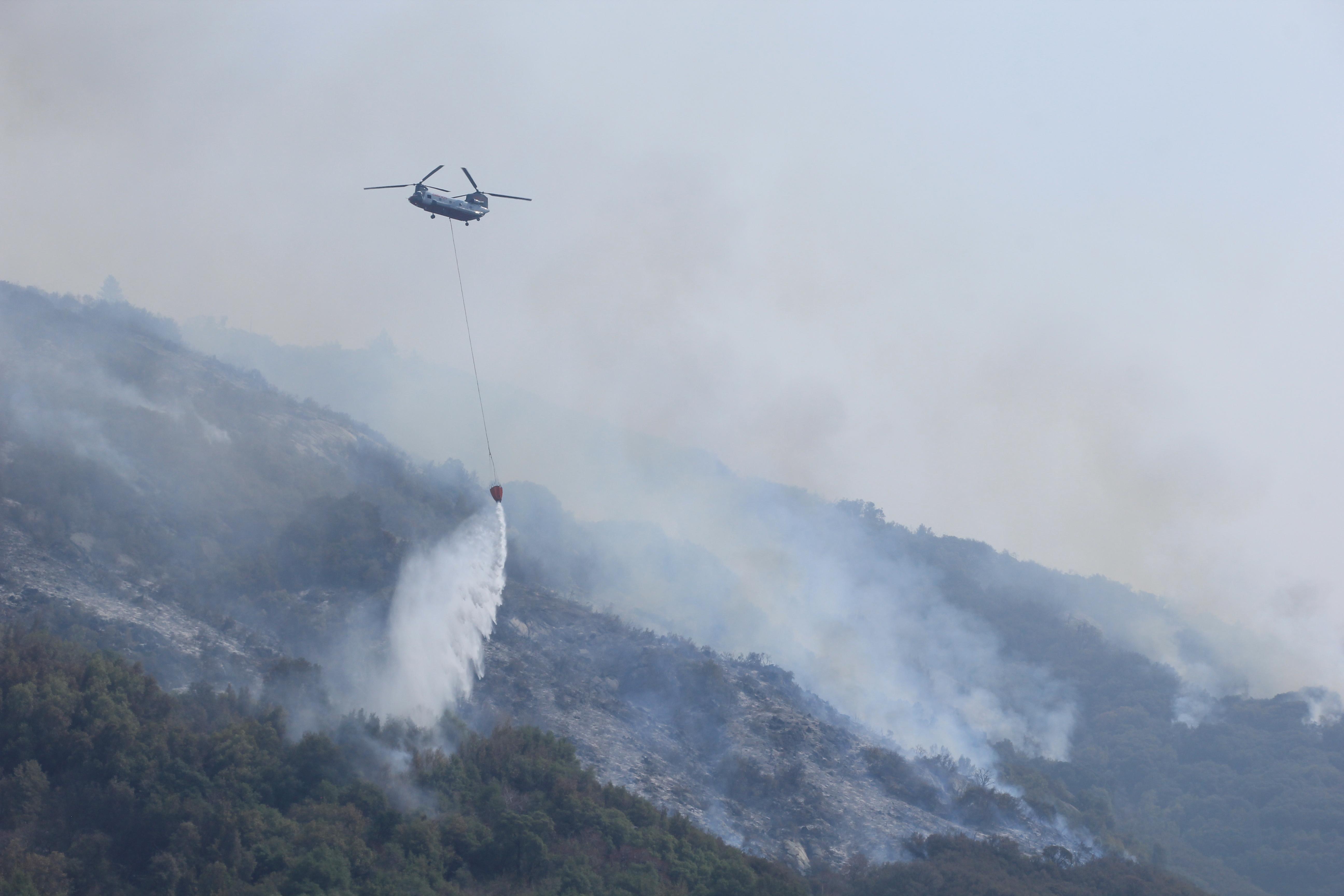 A grey Chinook helicopter drops water on the fireline high up on Paradise ridge