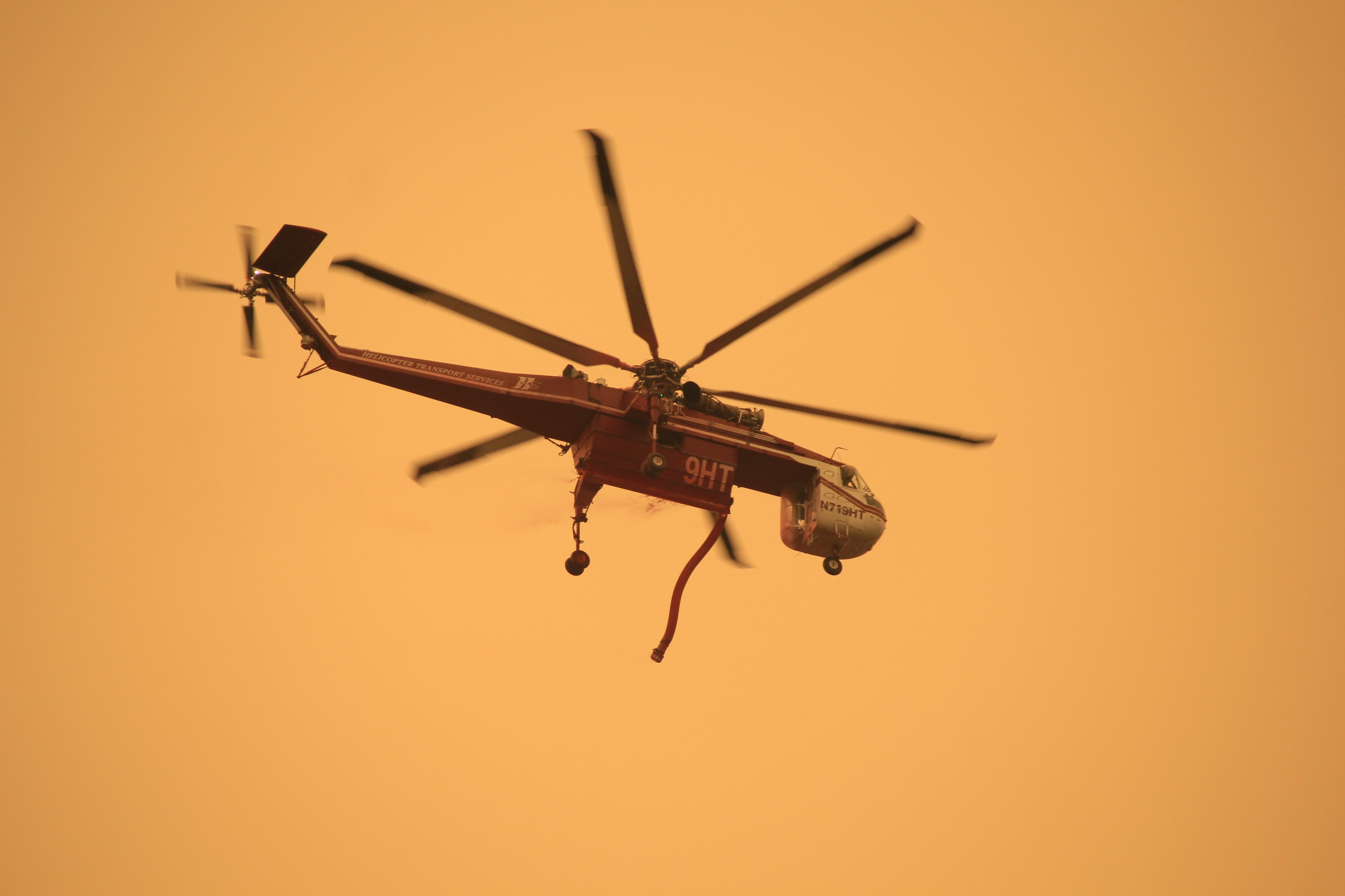 A helicopter with a hose flies in orange skies