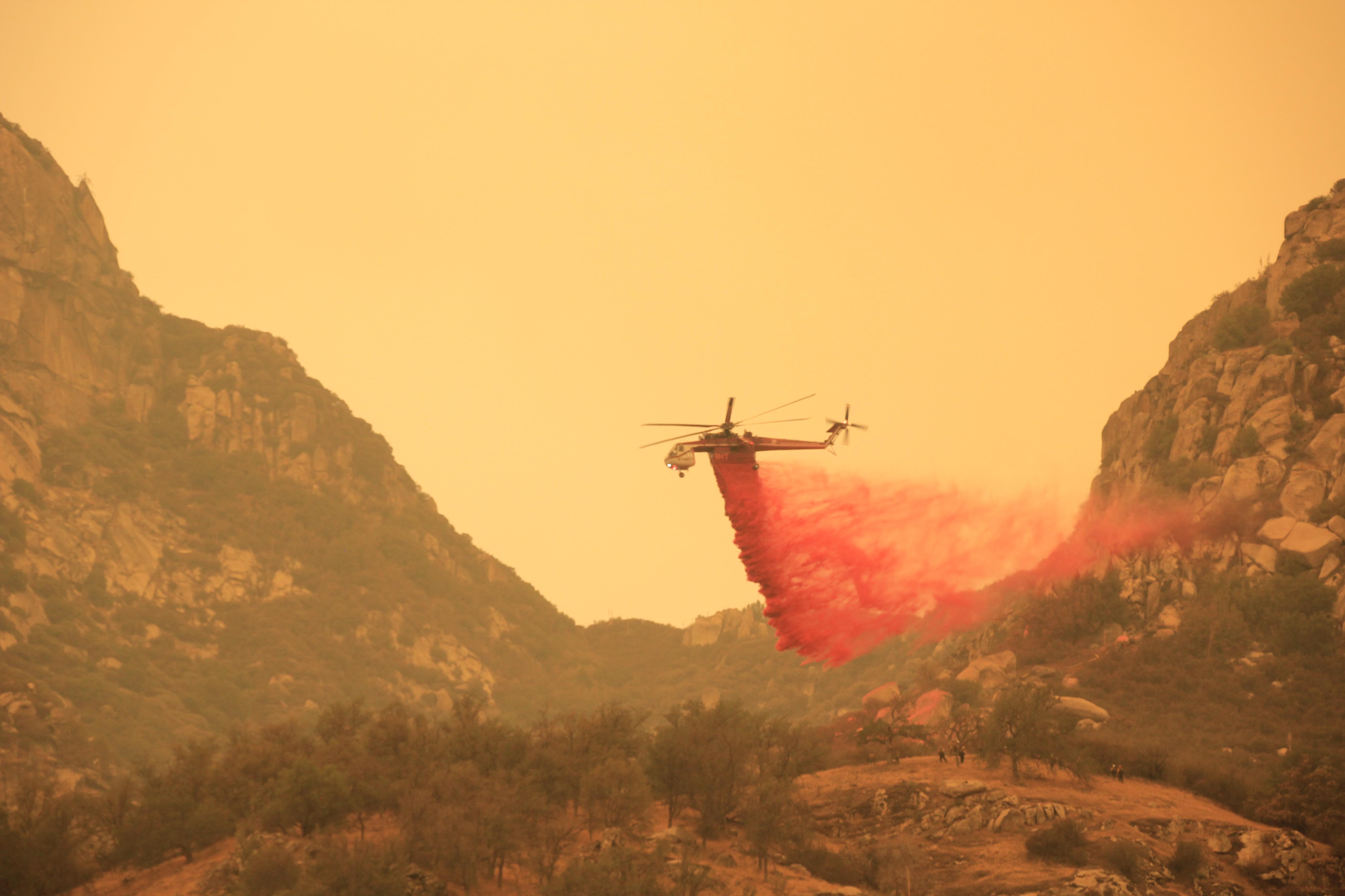 A helicopter drops red retardant across a valley