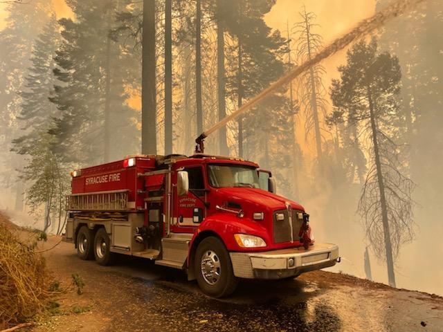 A red fire truck on a dirt road sprays water into a smoke-filled forest
