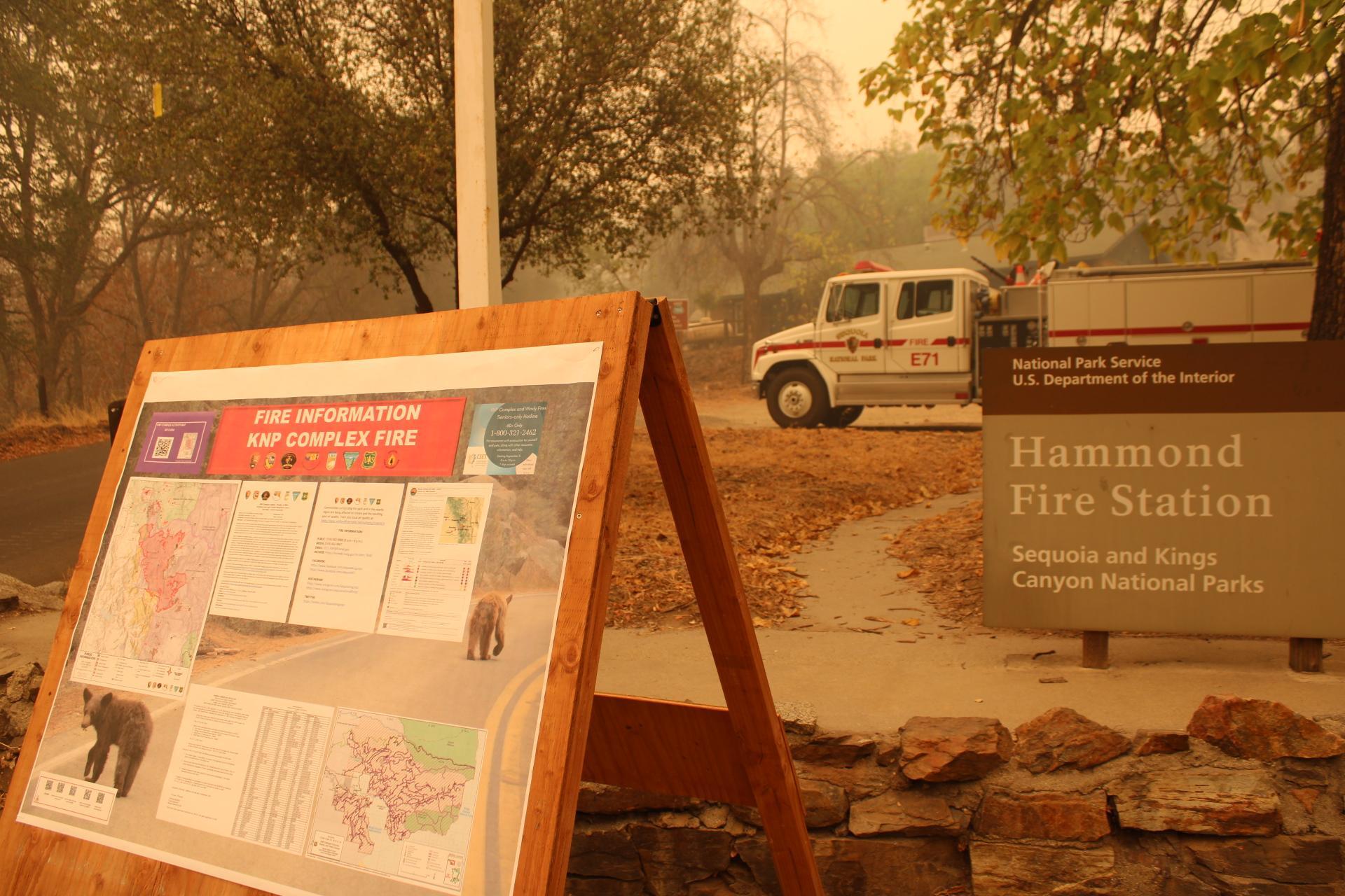 A wooden fire information board stands in front of a Hammond Ranger Station sign and white fire truck