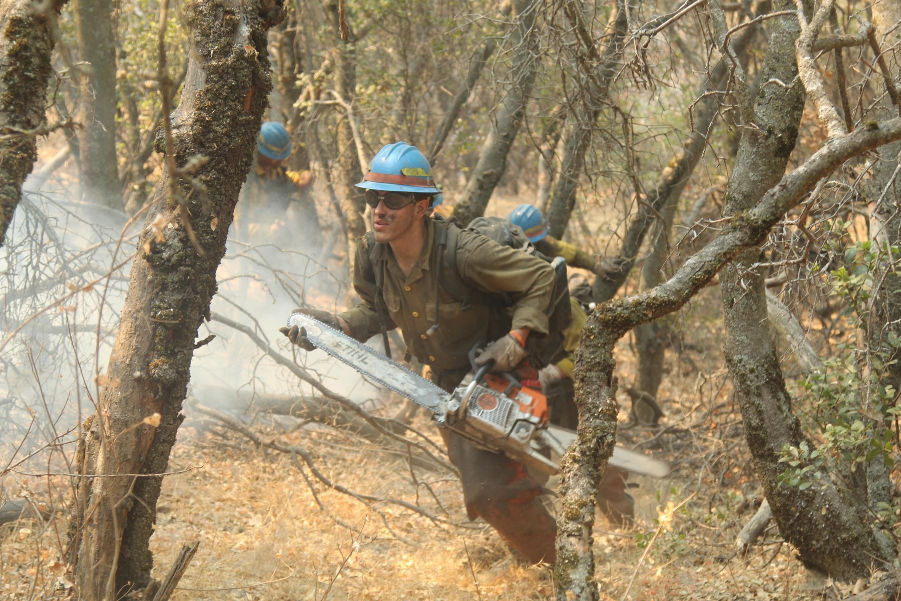 Firefighter hikes with a chainsaw to reach the fireline on the southwest flank.