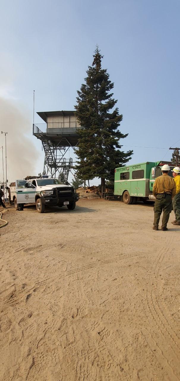 Fire crews and trucks gather underneath a metal fire tower