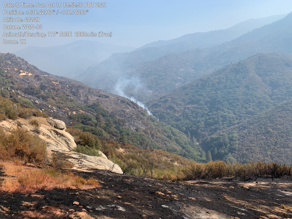 A column of smoke rises out of a valley with burnt ground