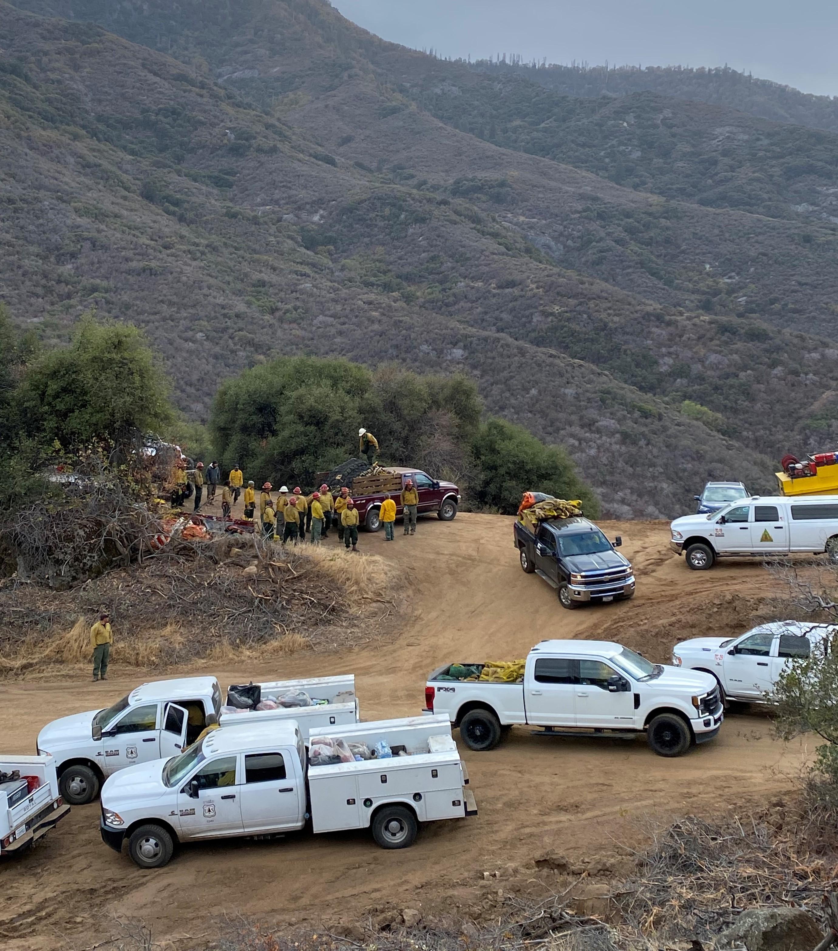Crews and trucks move around a staging area with a mountain in the background