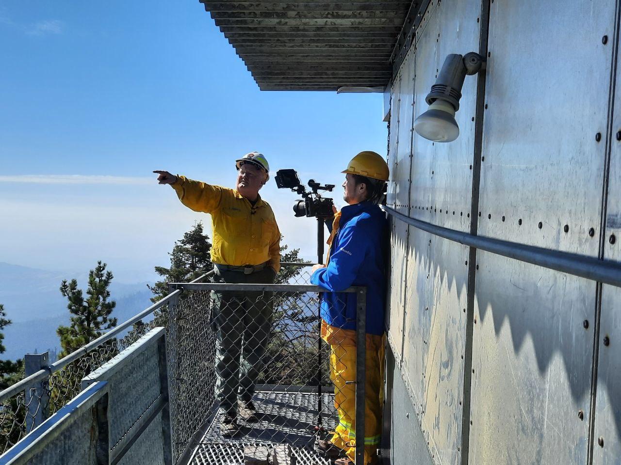 One person interviews another on top of a catwalk on a fire tower