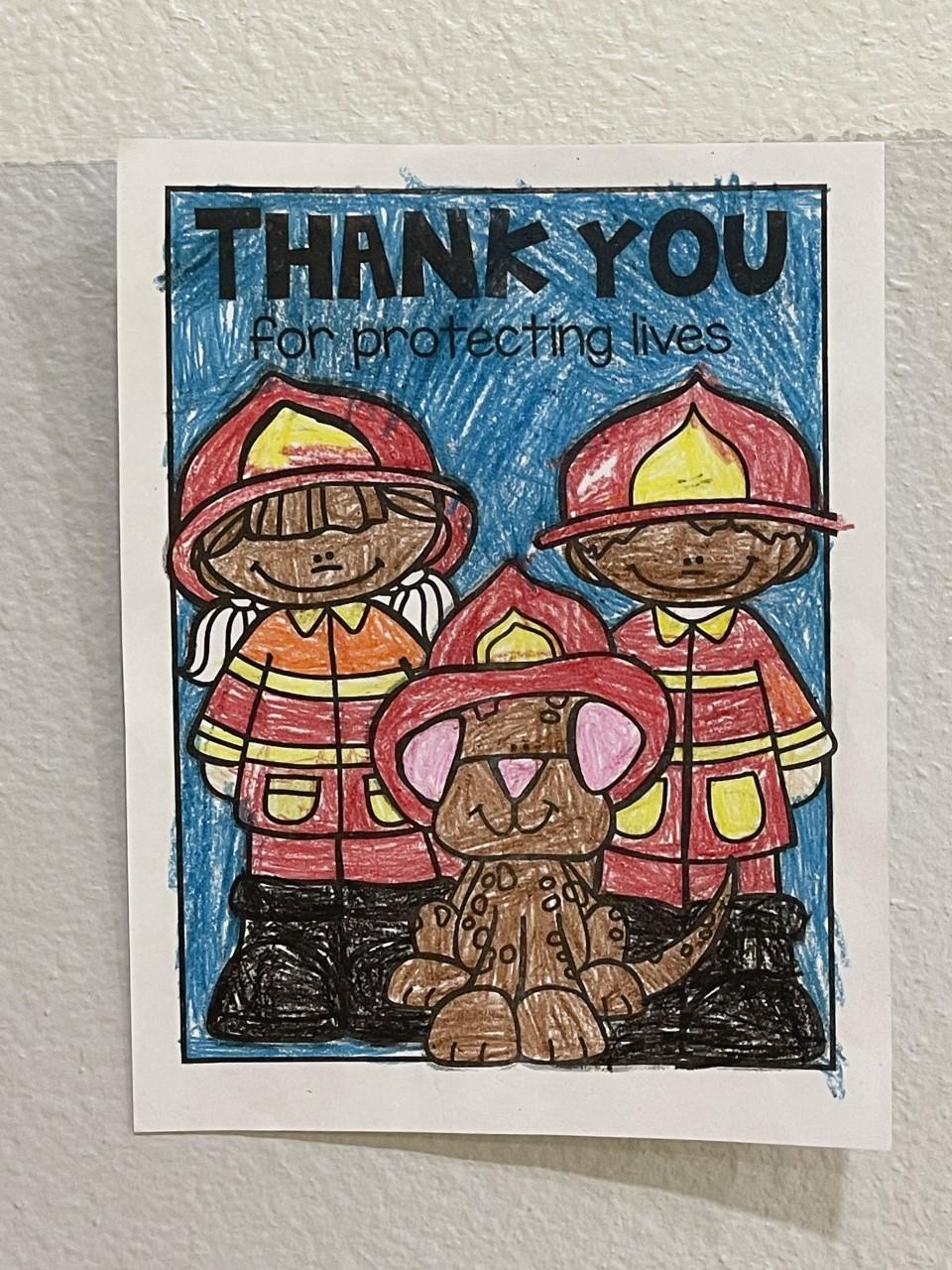 A special crayon colored page of 2 firefighter s and a dog from an elementary student