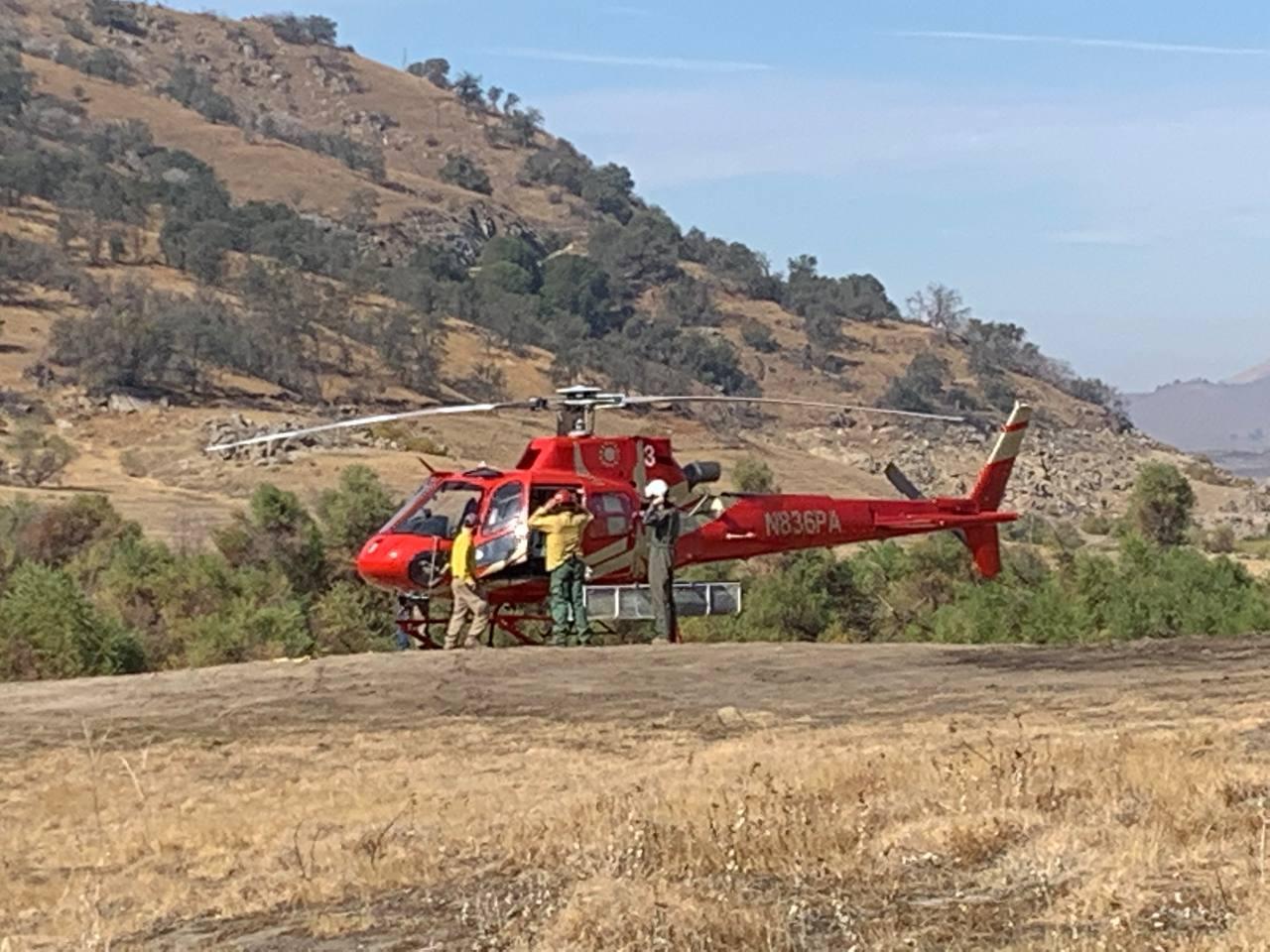 A red and gold helicopter with three firefighters standing nearby