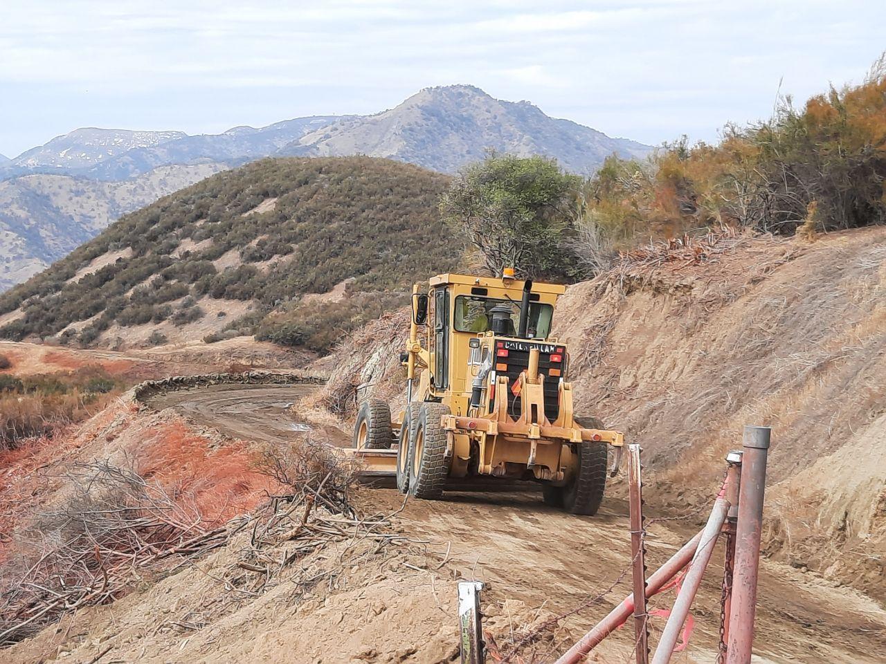 A road grader, piece of heavy equipment, working on dirt road to maintain safe passage for firefighting resources.