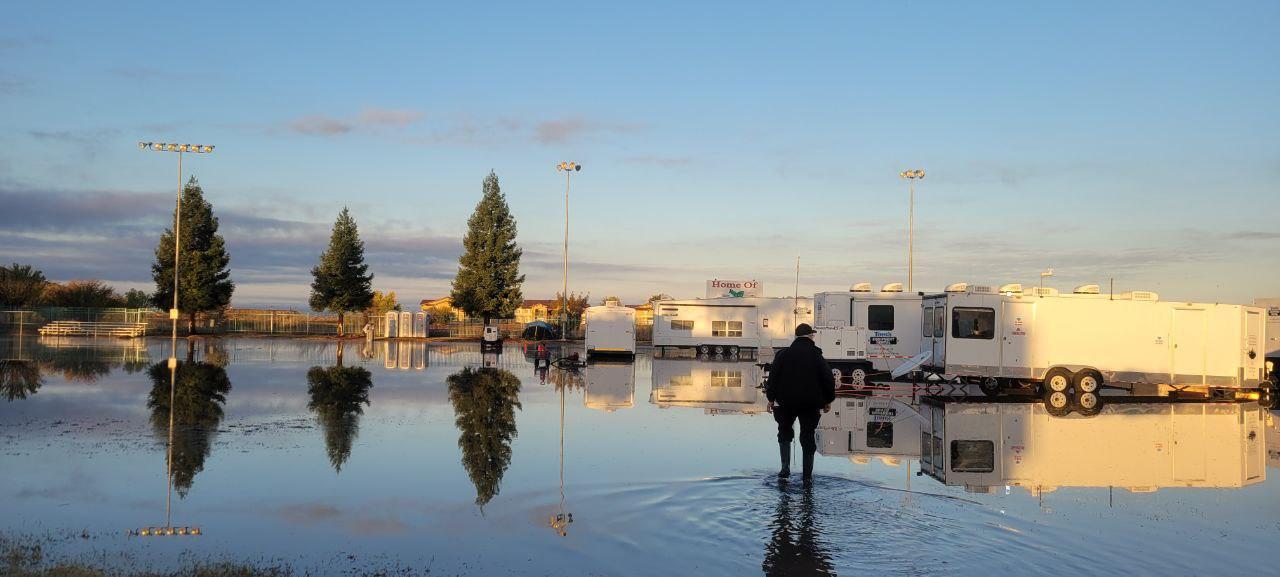 Multiple white travel trailers surrounded by water in the early morning.  Man walking through water, away from camera
