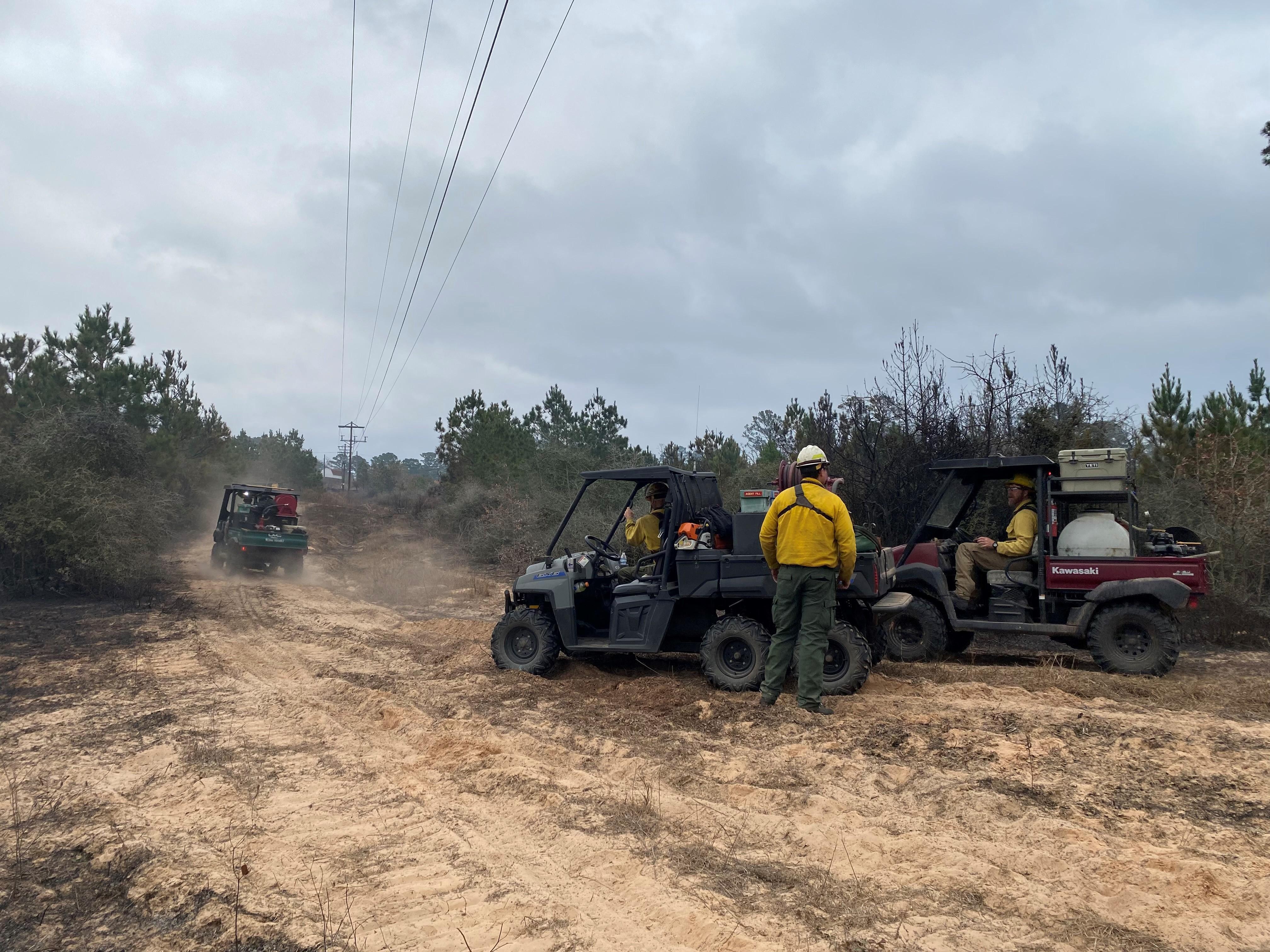 View of fireline personnel patrolling a containment line using UTVS alone a powerline