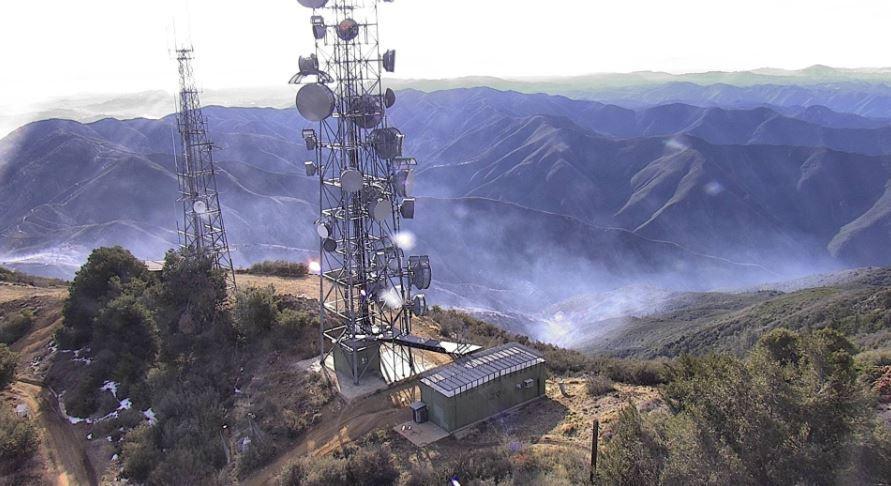 Very light smoke rising from burned hillside in background of communications towers.