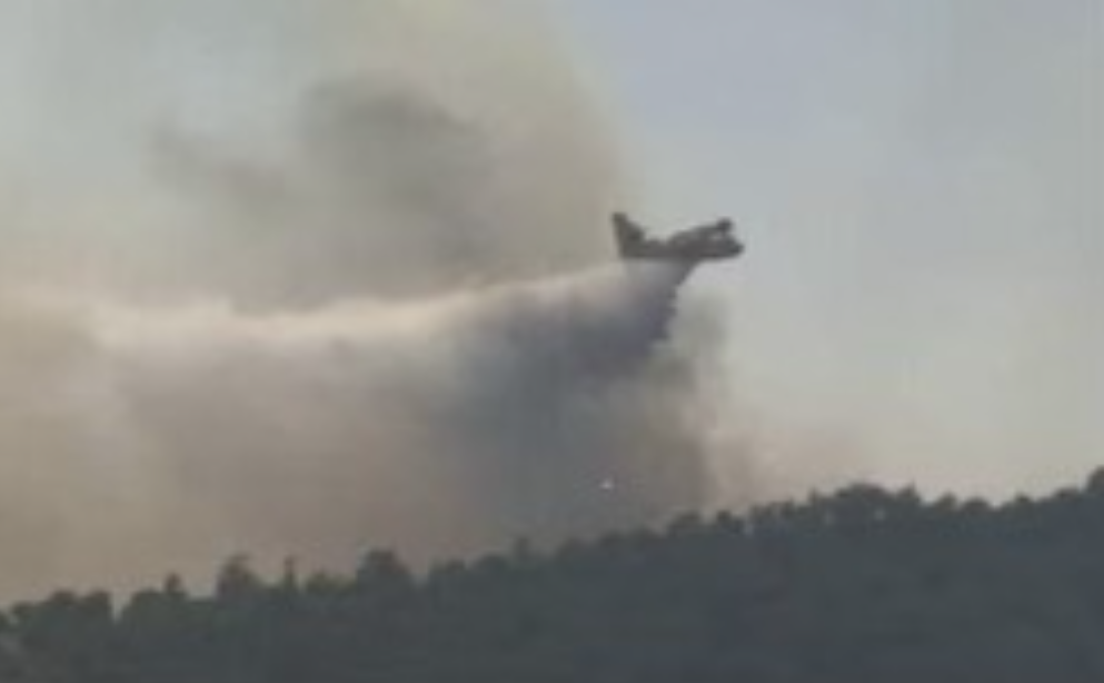 zoomed in shot of a plane dropping water on a smoke covered ridge