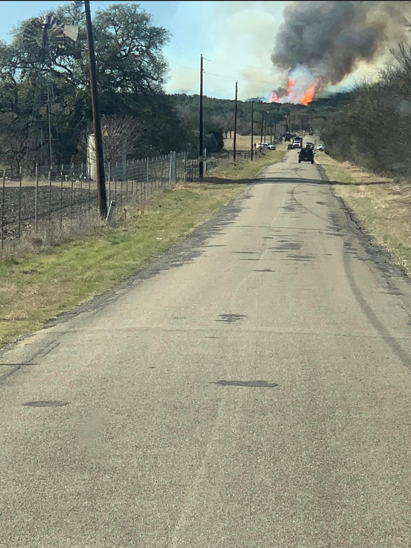 view down a county road with tall flames and black smoke on the next ridge line over.