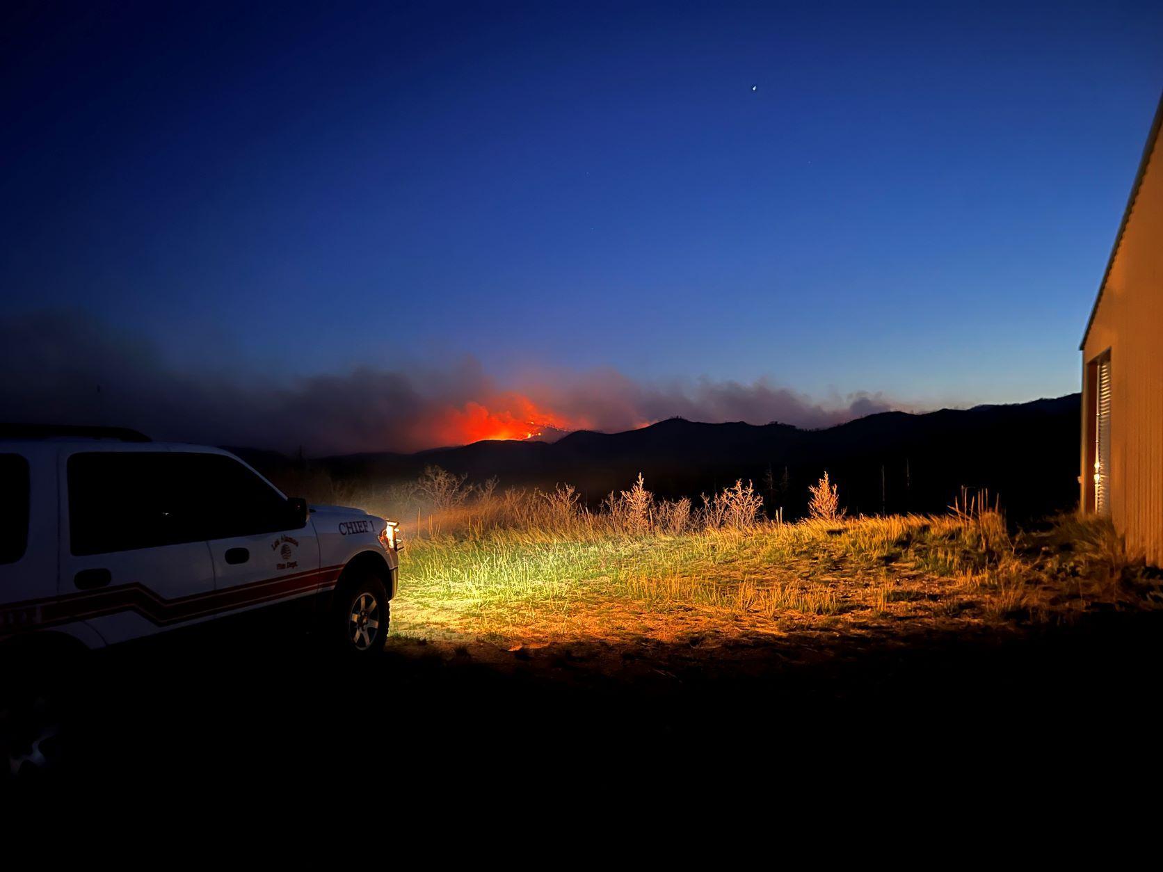 Fire glows in the distance with a fire vehicle in the foreground.