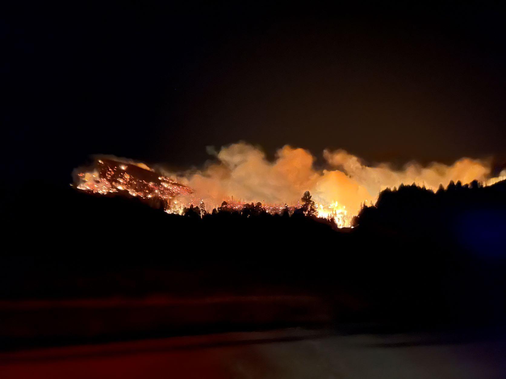Fire burns at the base of a mountain at night