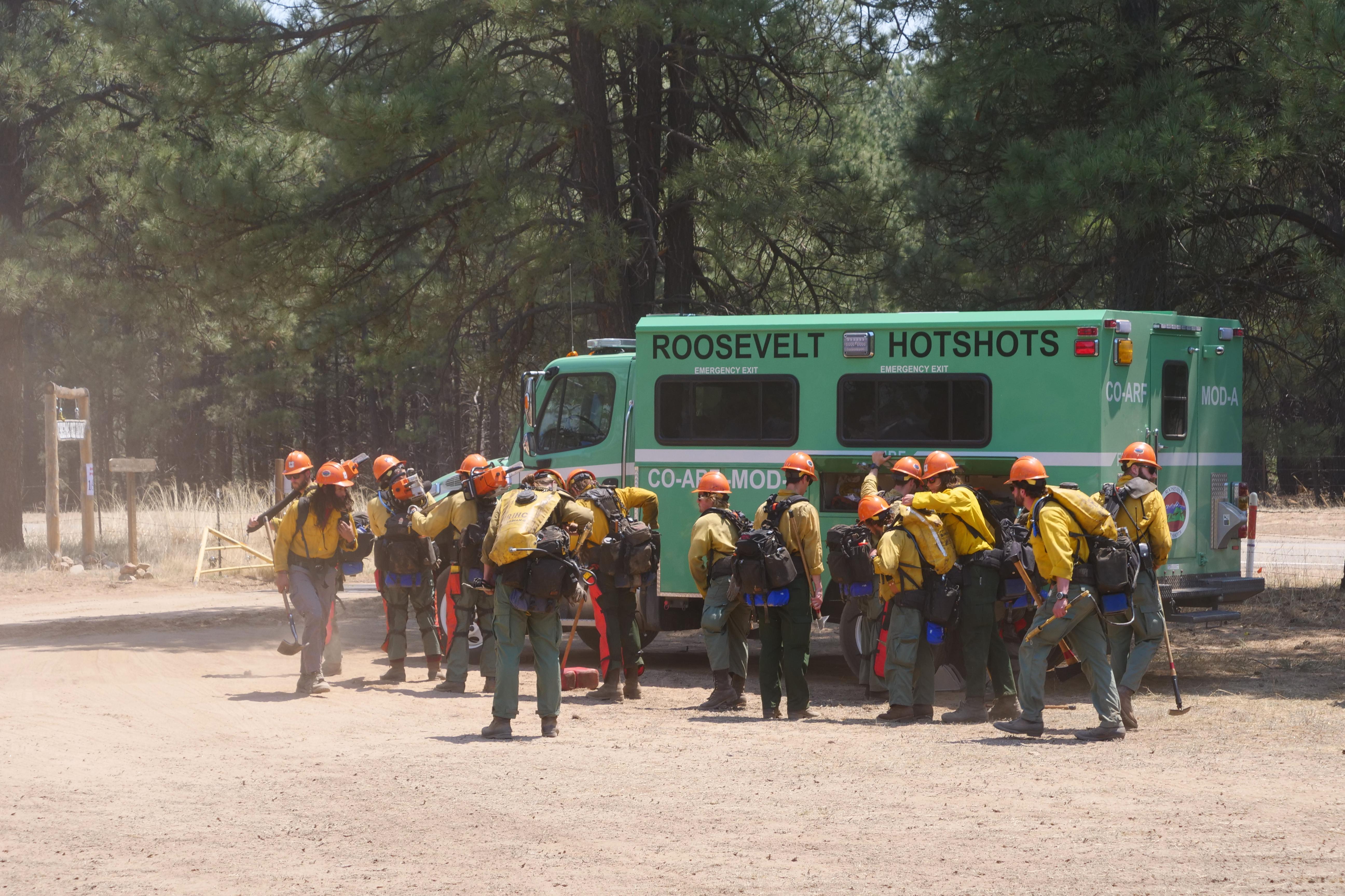 A group of firefighters in yellow shirts, orange helmets and other protective gear prepare to fight a forest fire.