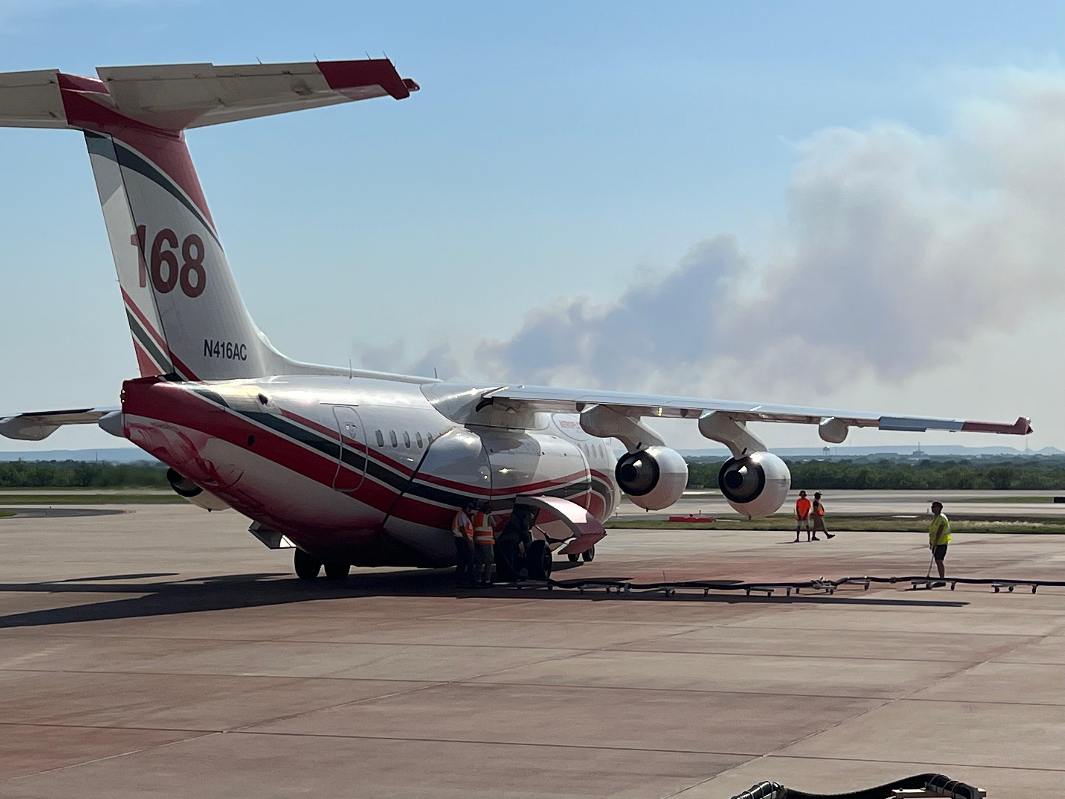 A large airtanker reloads with fuel and retardant before responding to the Mesquite Heat Fire, which can be seen in the background on May 17, 2022