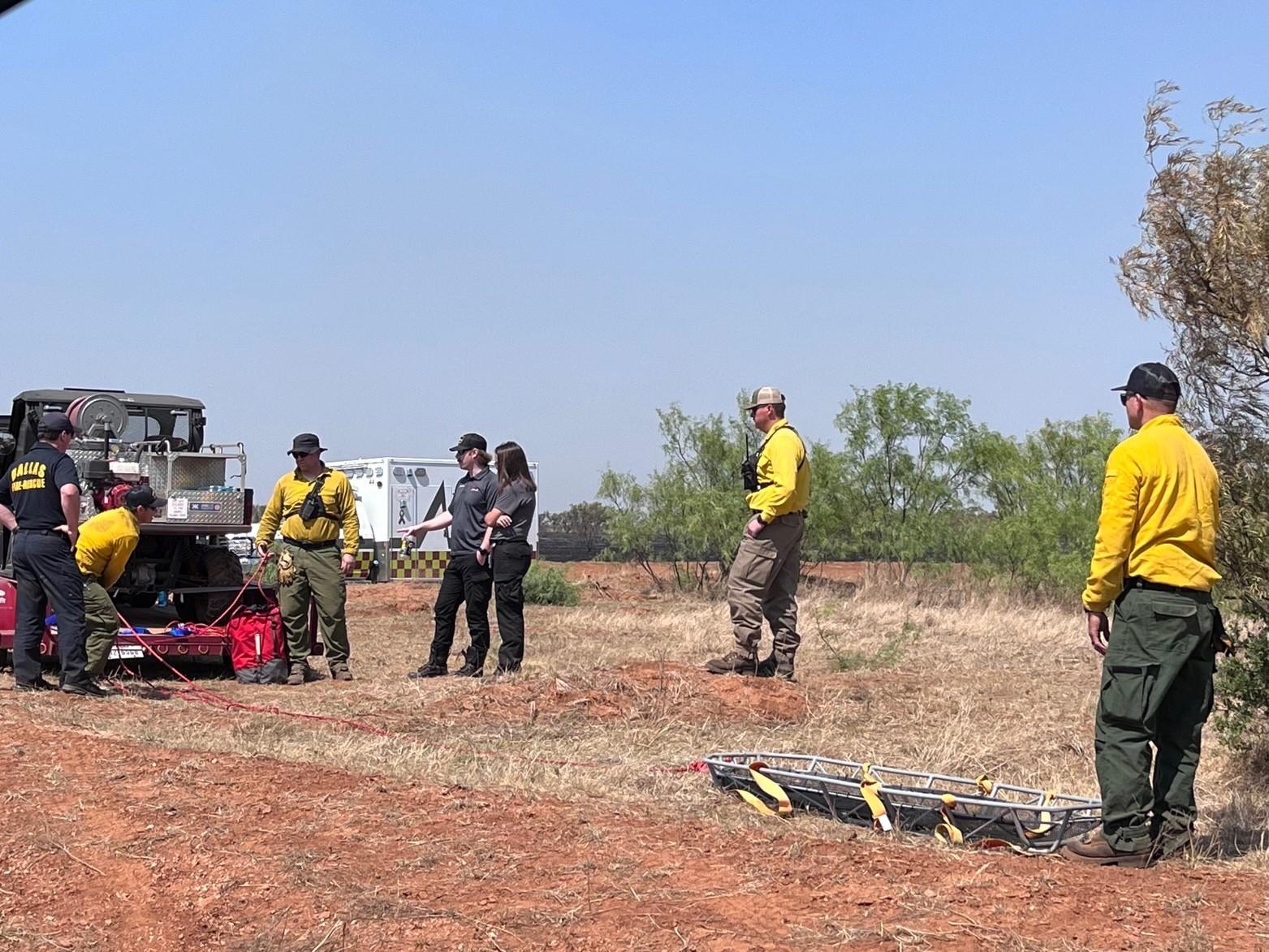 group of fire fighters and emergency medial personnel standing on and around a trailer containing an UTV,. personnel is going over their equipment