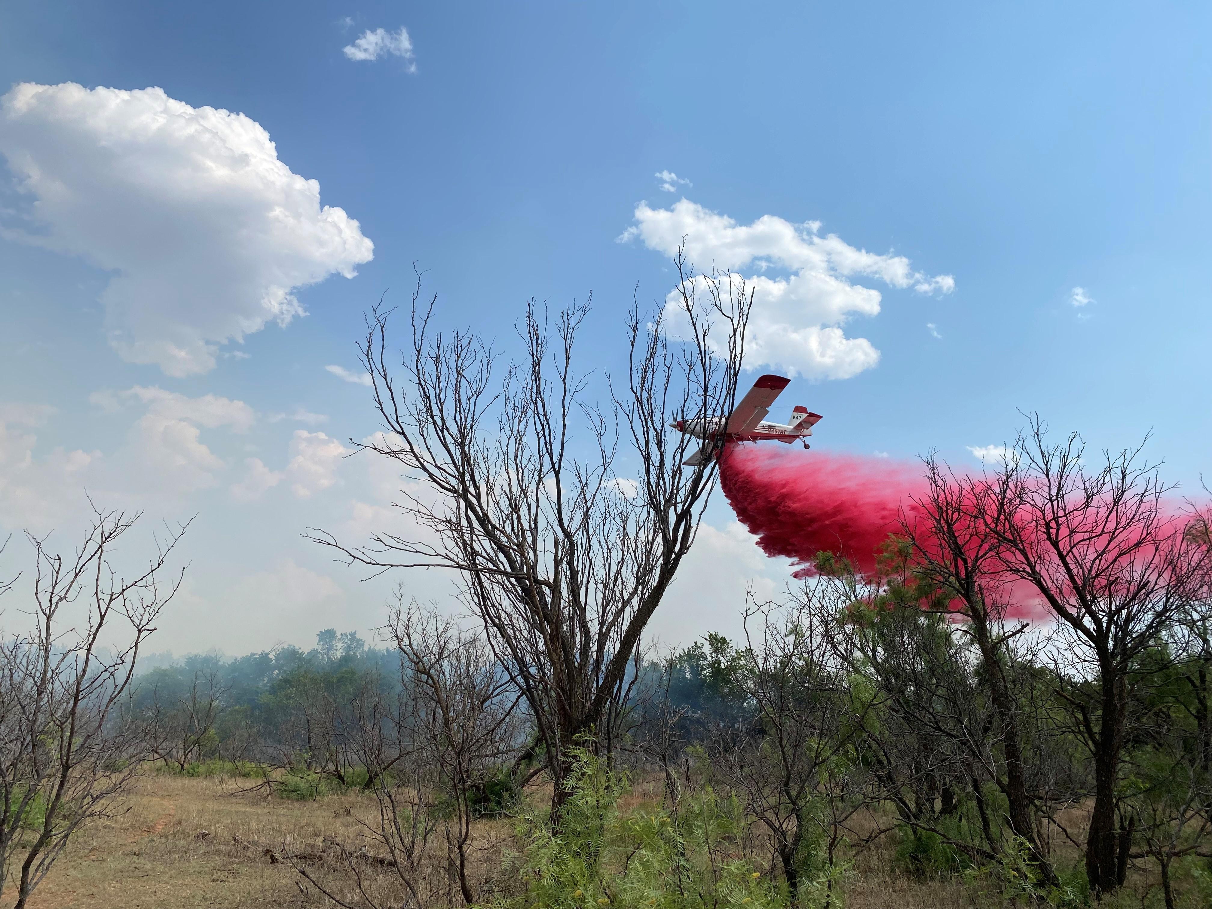 airplane is flying towards the left and there is pink liquid substance called retardant, on top of the active fire.