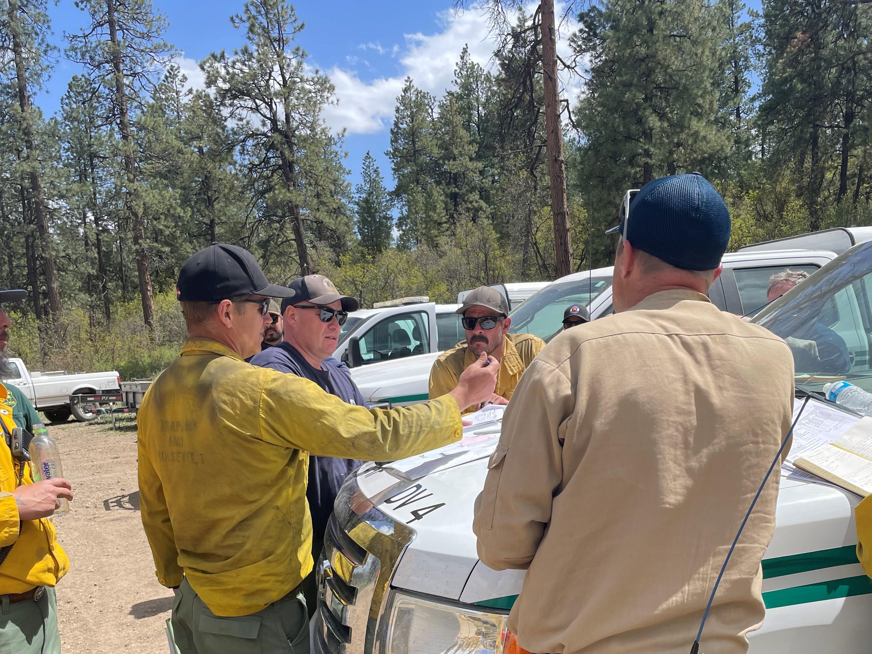 Members of the incident management team talk about fire progress while looking at a map on the hood of a pickup truck. 