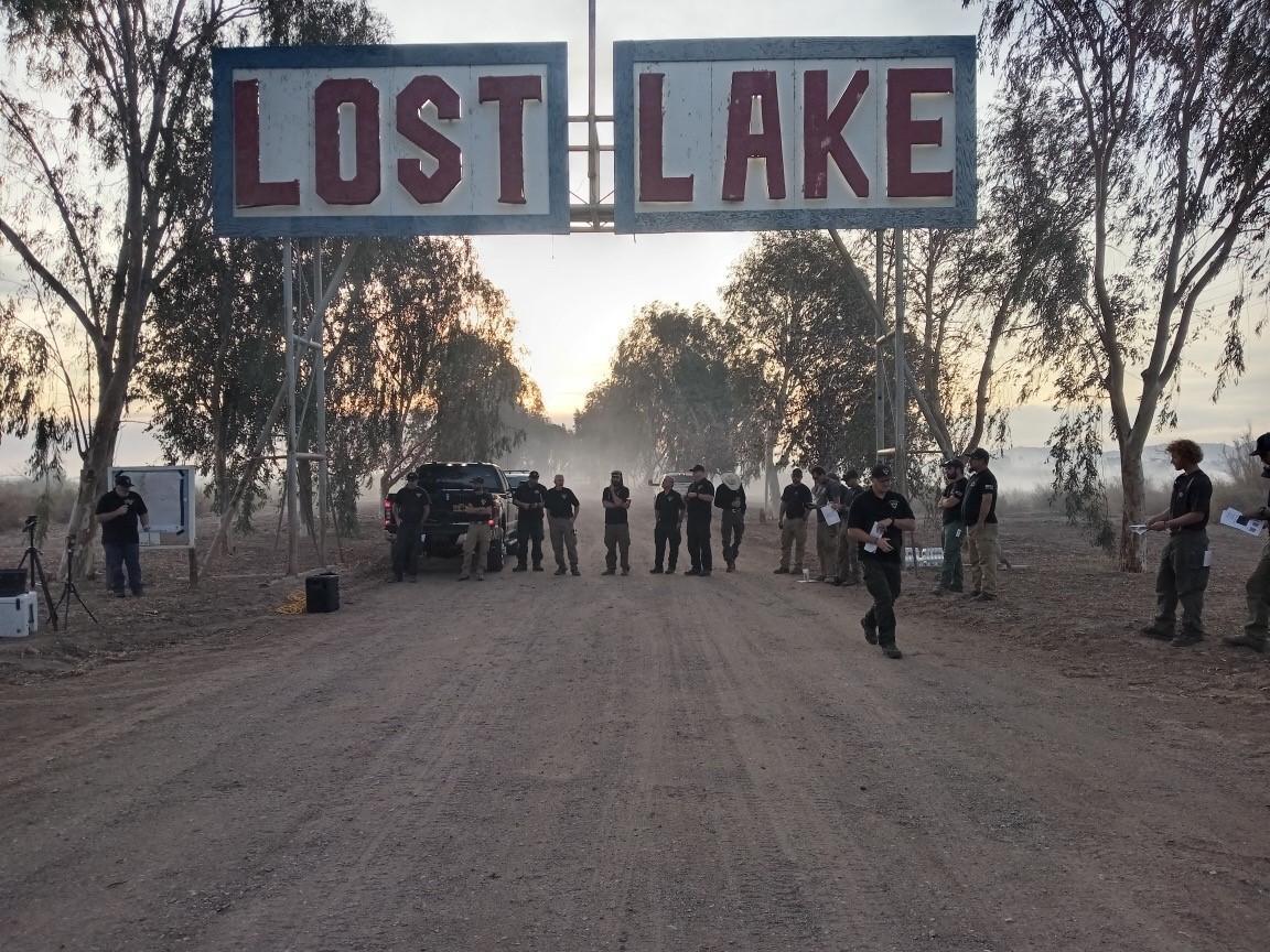 A sign hung over a dirt road where firefighters are standing reads Lost Lake