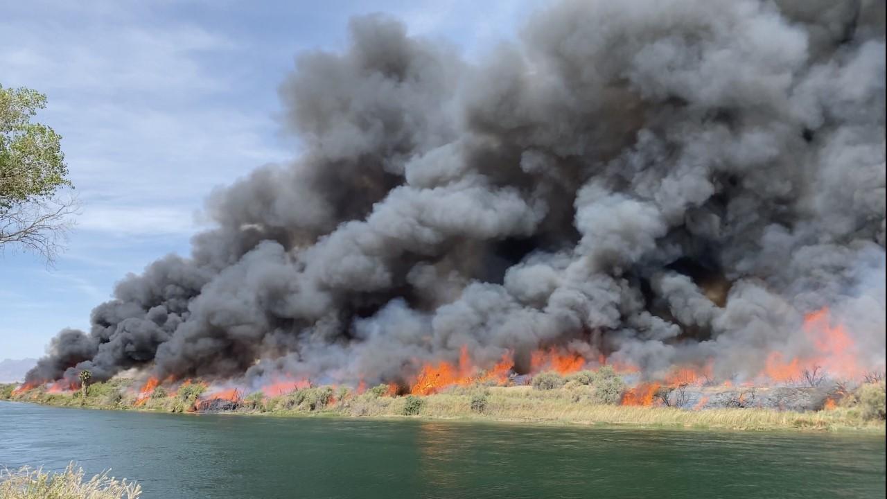 Black smokes rises over water with a thin band of orange flames in the middle