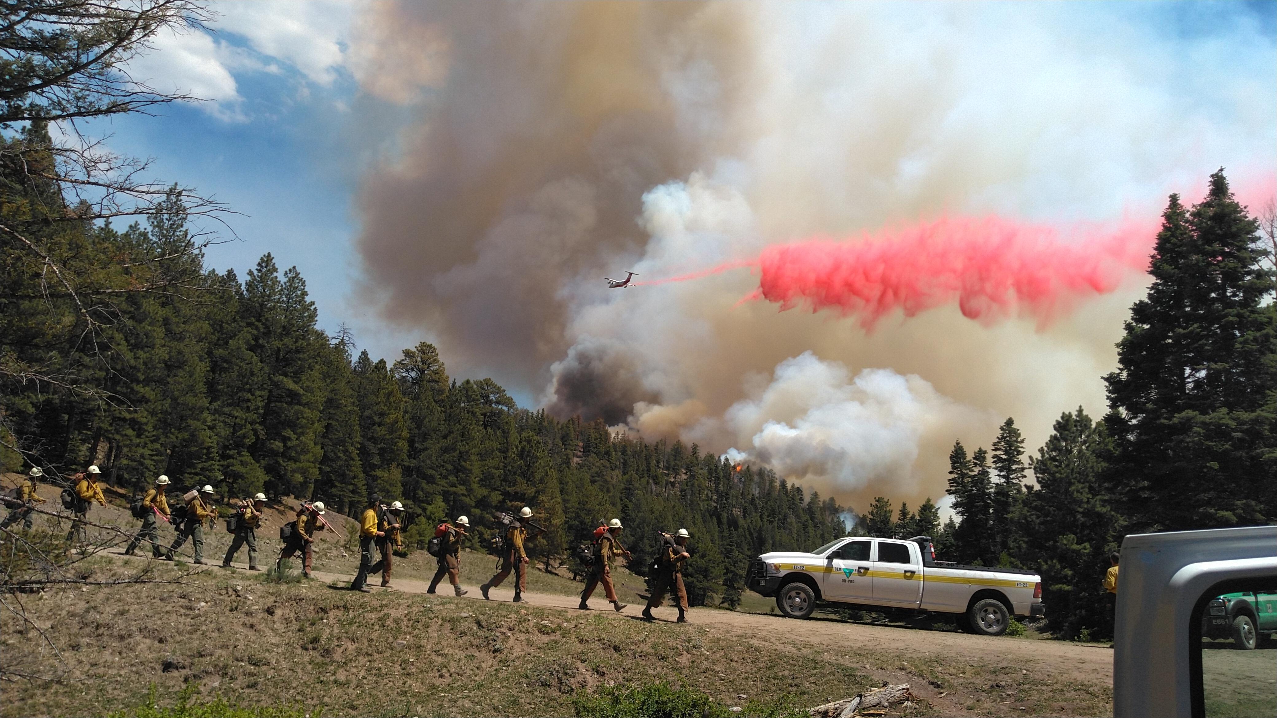Fire crew walking to rally point as fire retardant is dropped overhead