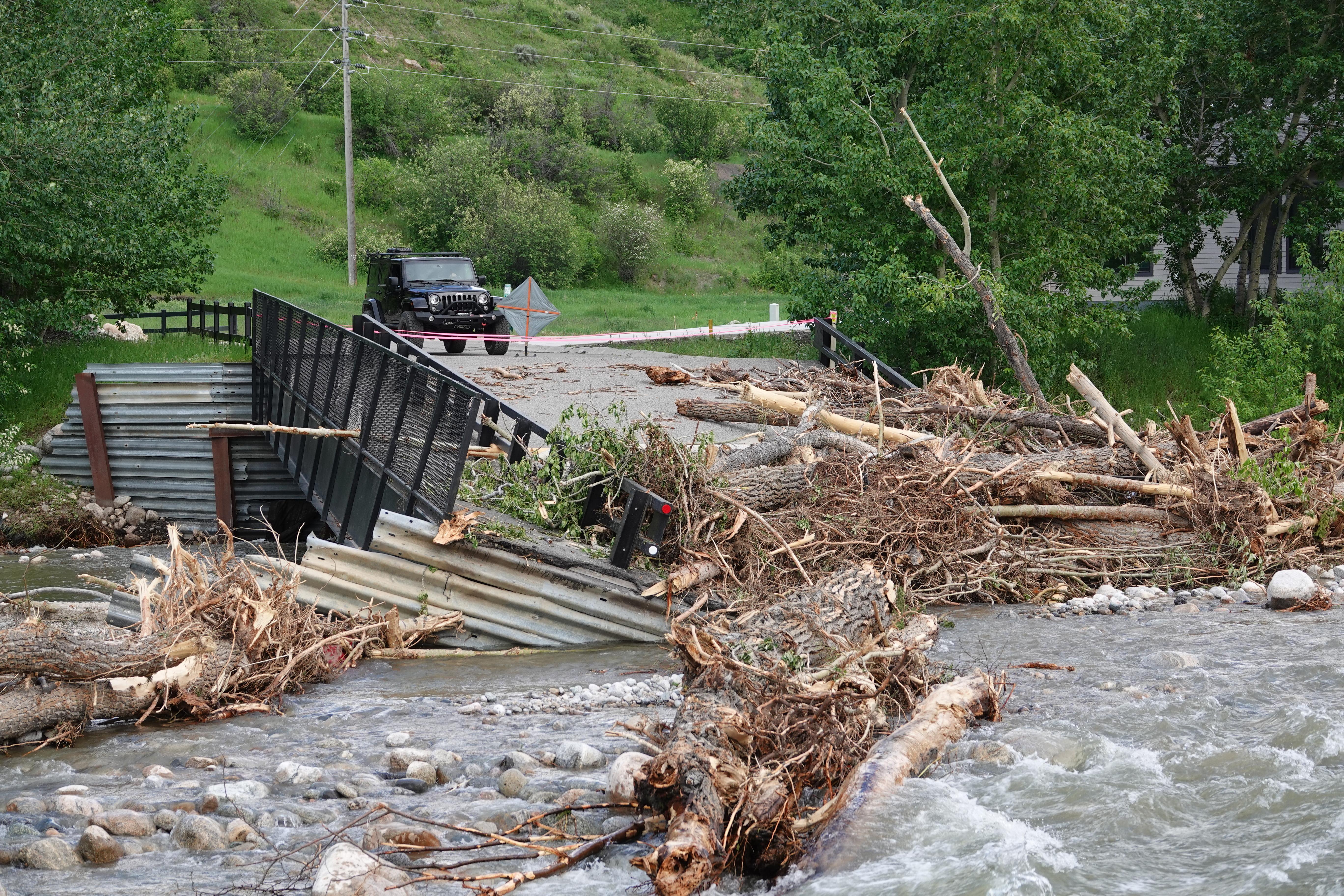 Rapidly flowing creek with bridge out; damaged bridge and debris on both sides of creek