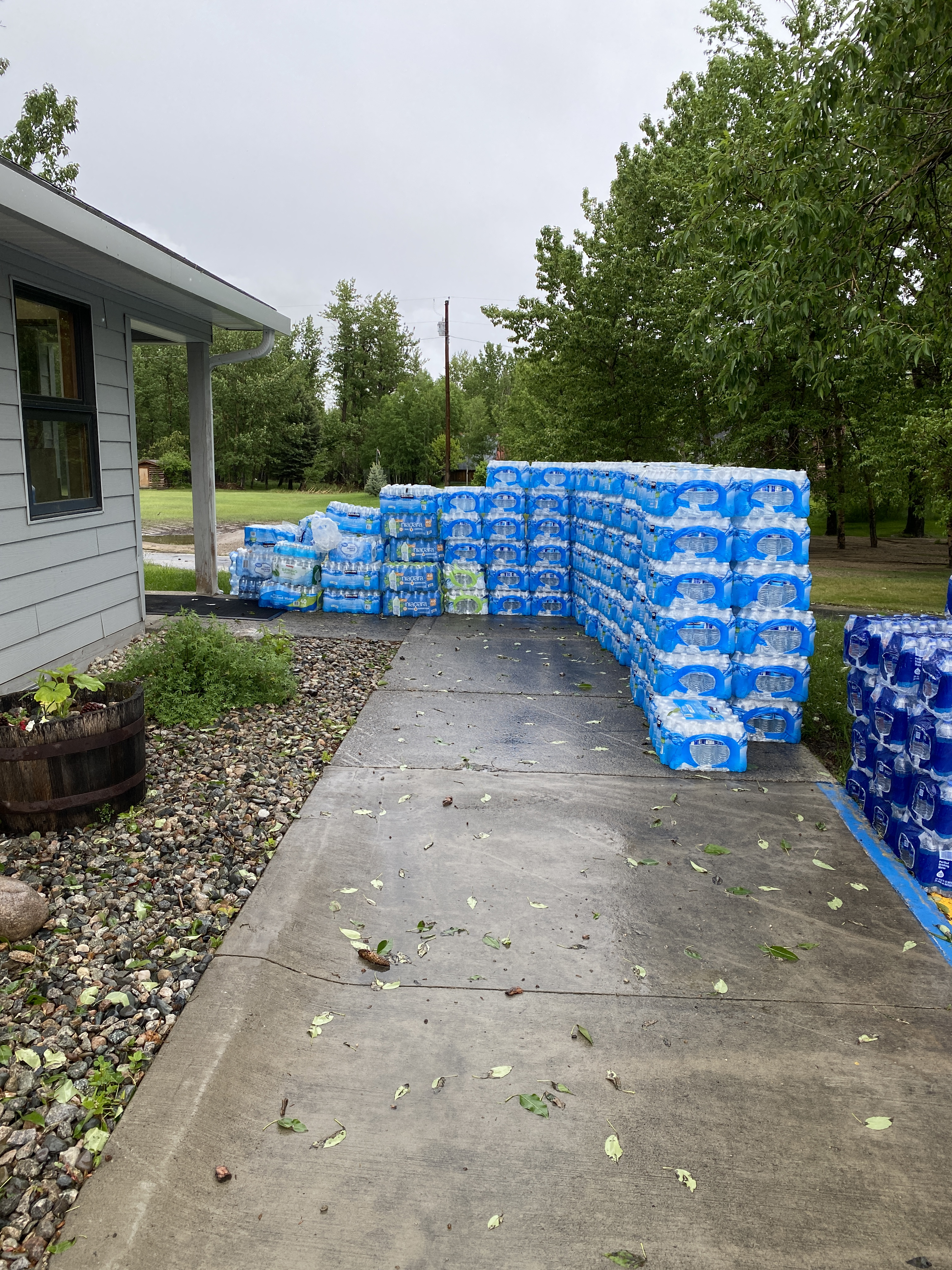 Cases of water stacked near a building on concrete sidewalk