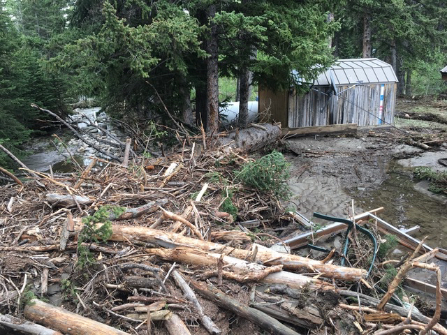 Pile of limbs and branches amidst flood waters with wood shed in background