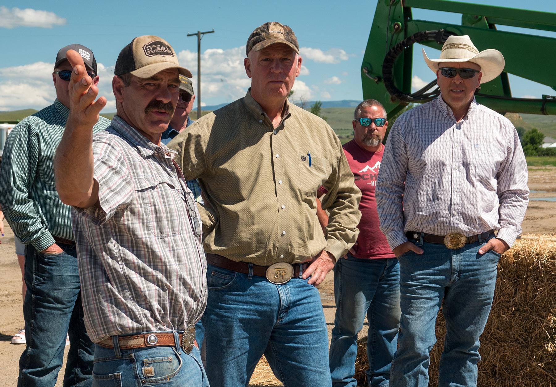 Rancher screen left pointing, Governor and Commissioner in photo. Heavy equipment in background.