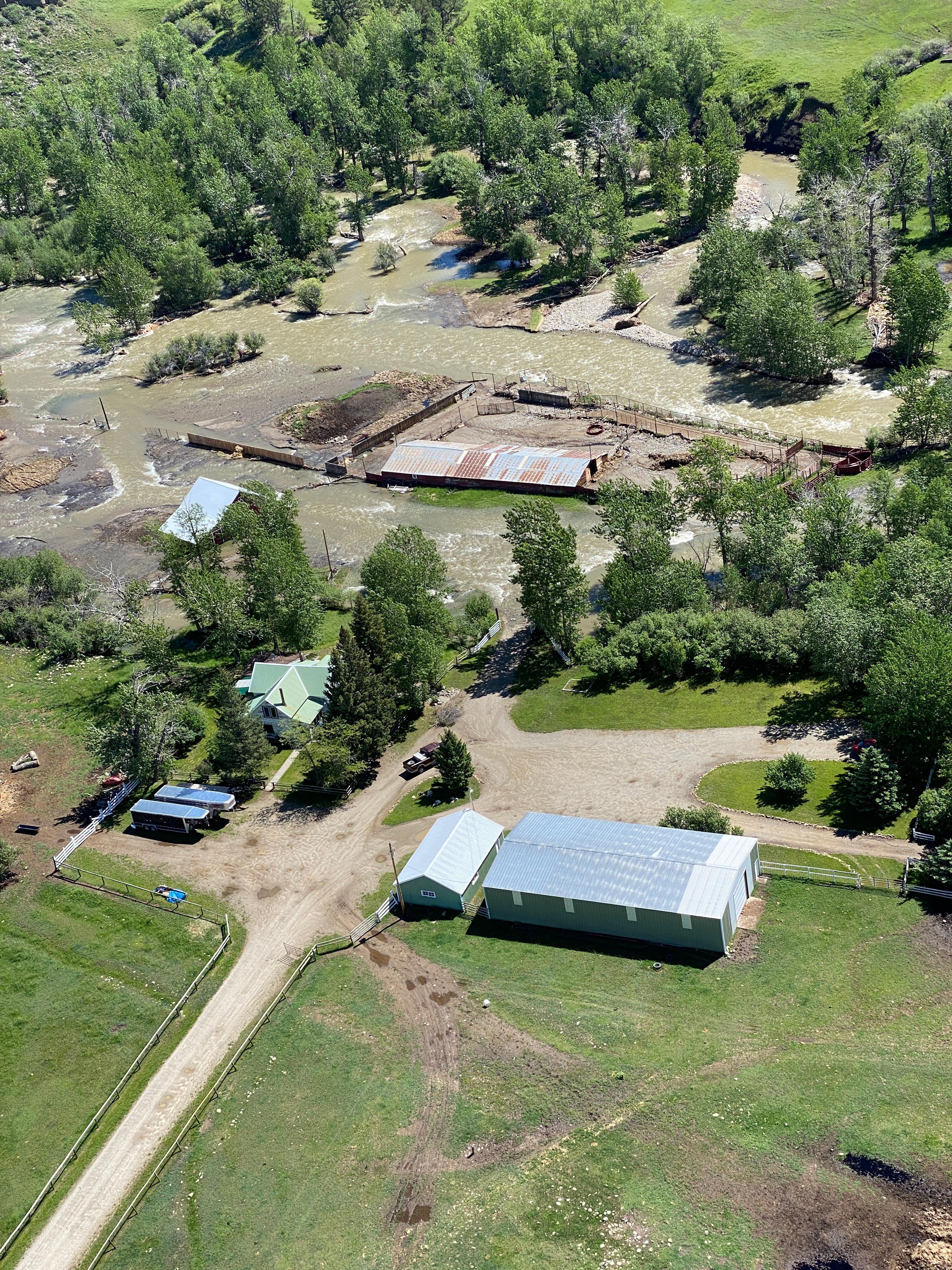 River out of its banks running from upper right to lower left. Some partially submerged farm buildings in upper portion of image; partially submerged, broken roof center left.