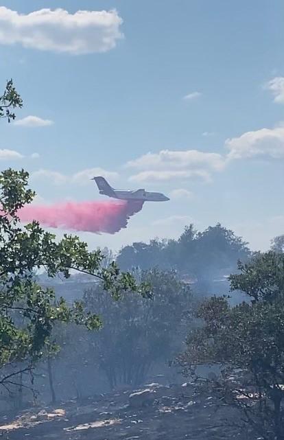 A large airtanker, white and red with the number 40 on the tail, drops red retardant on vegetation with smoke