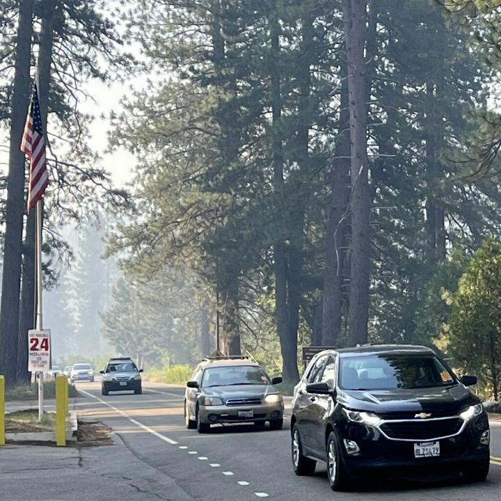 Photo shows cars traveling down a forested two land road as they reenter the Wawona Area.