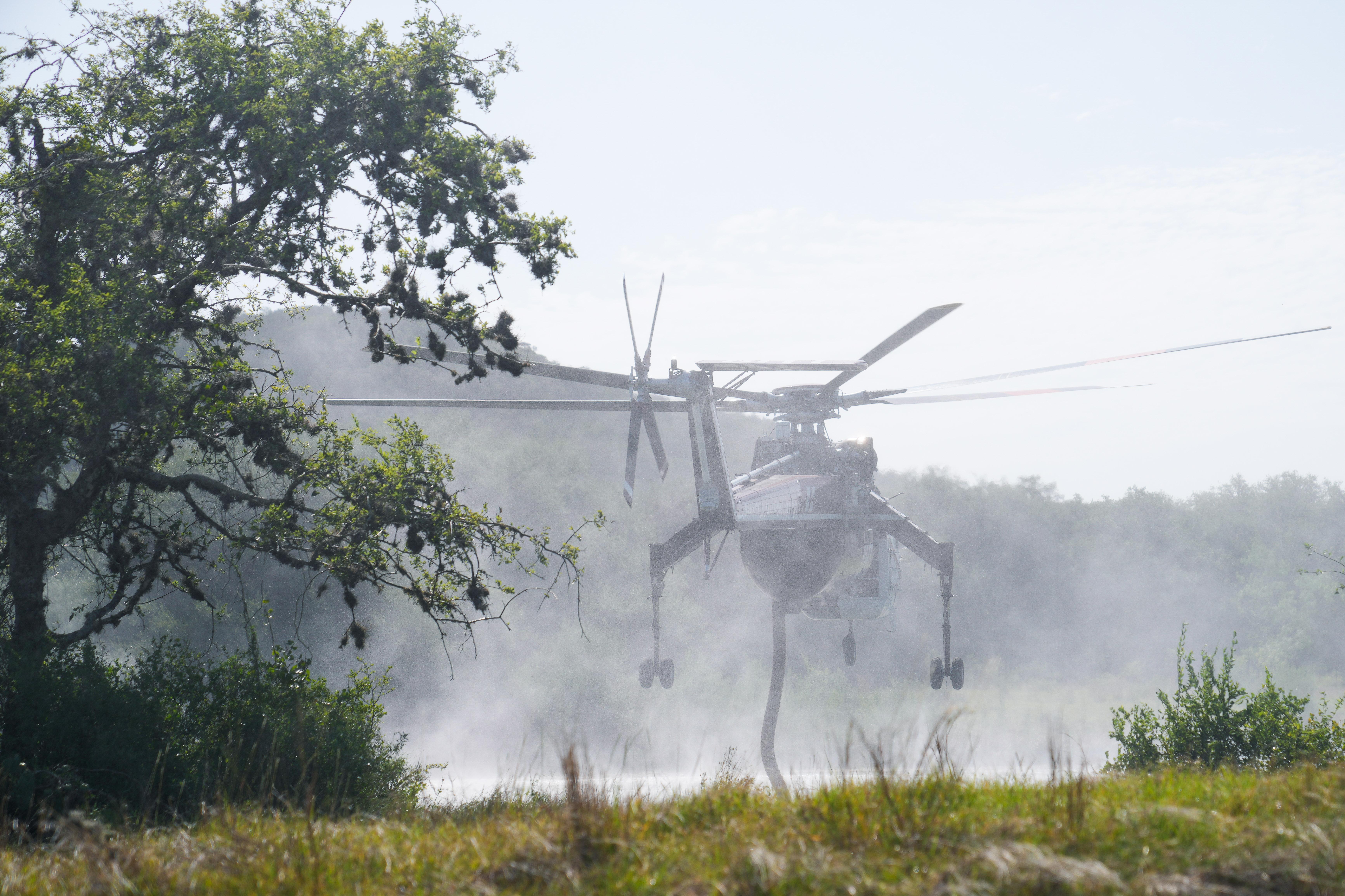 A heavy helicopter hovers above a pond while it sucks water into its holding tank.