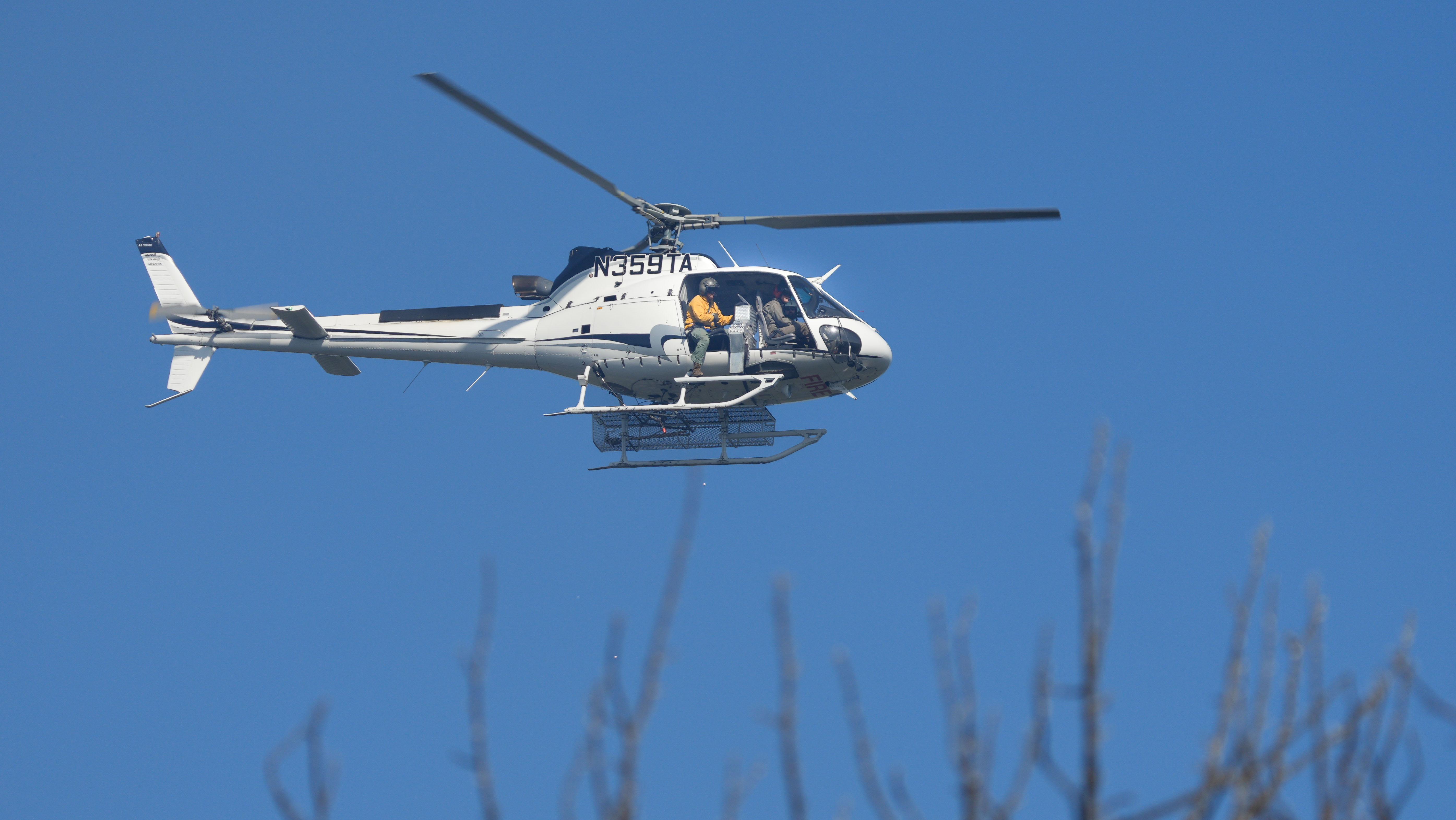 Helicopter flying low with an operator and dispenser in the doorway