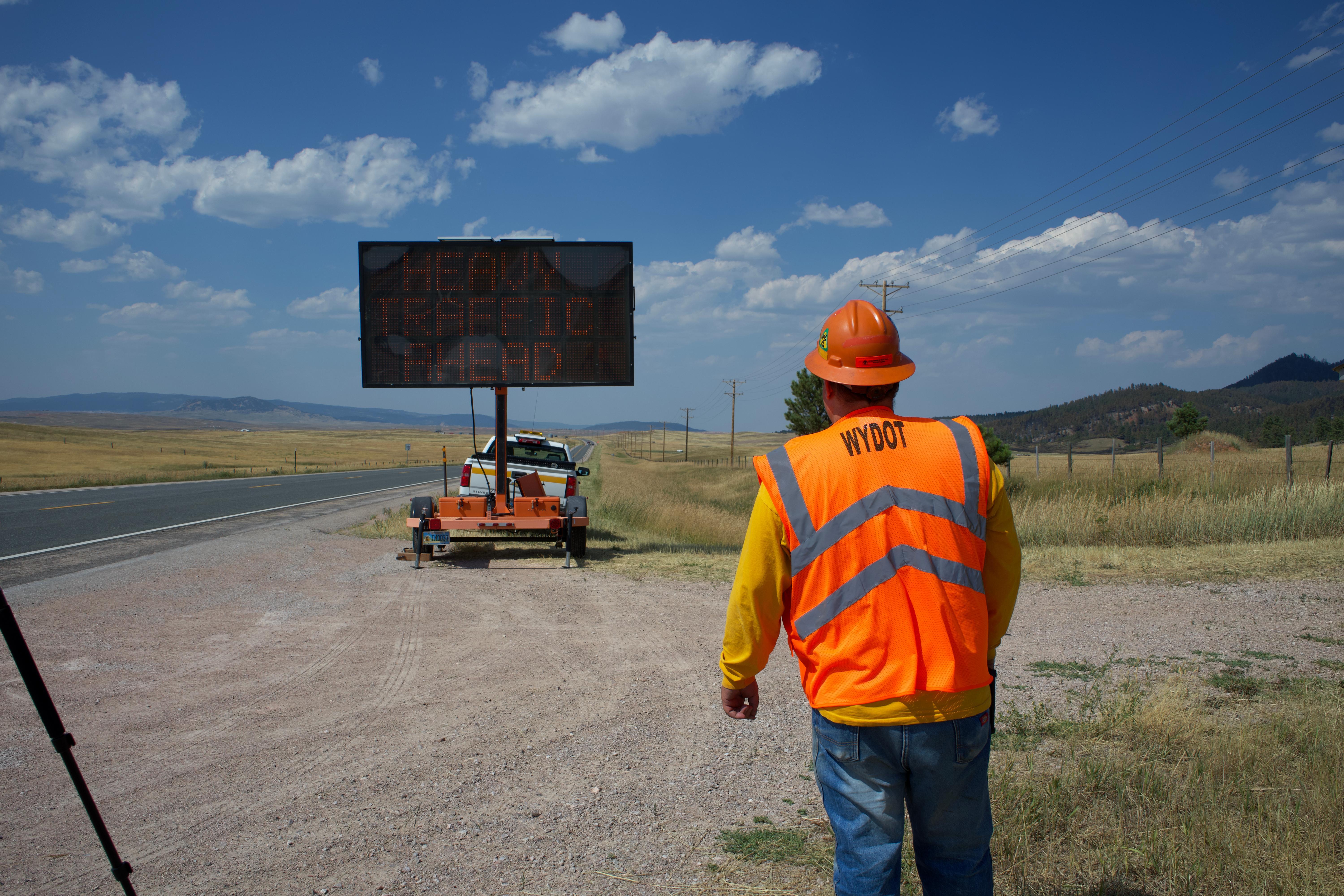 A highway worker installs a large electronic hazard warning sign on the side of the road to warn motorists of fire equipment along the road