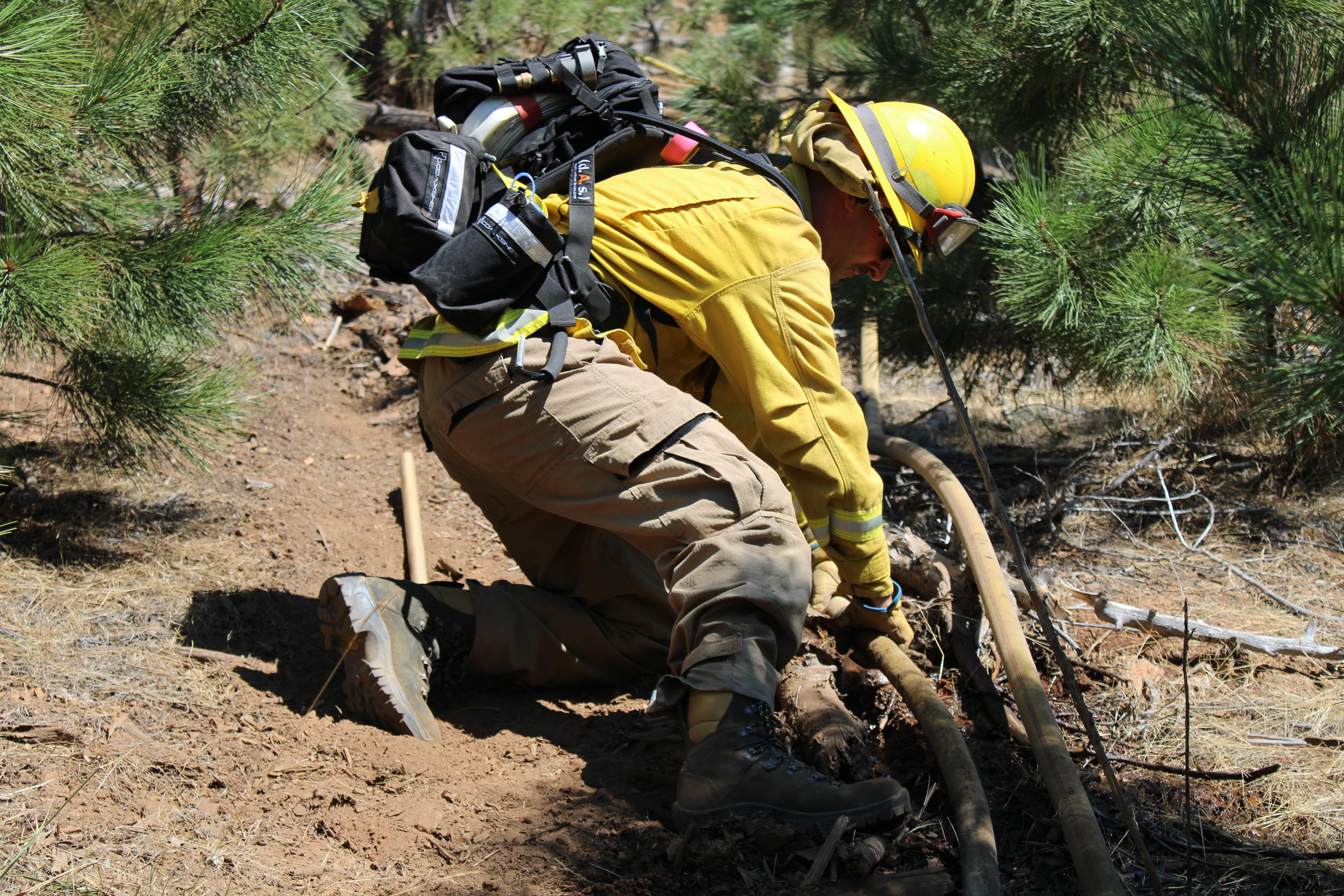Antelope Valley Fire crewmember repairing hose on hillside supplying crews mopping up Smokey Fire  