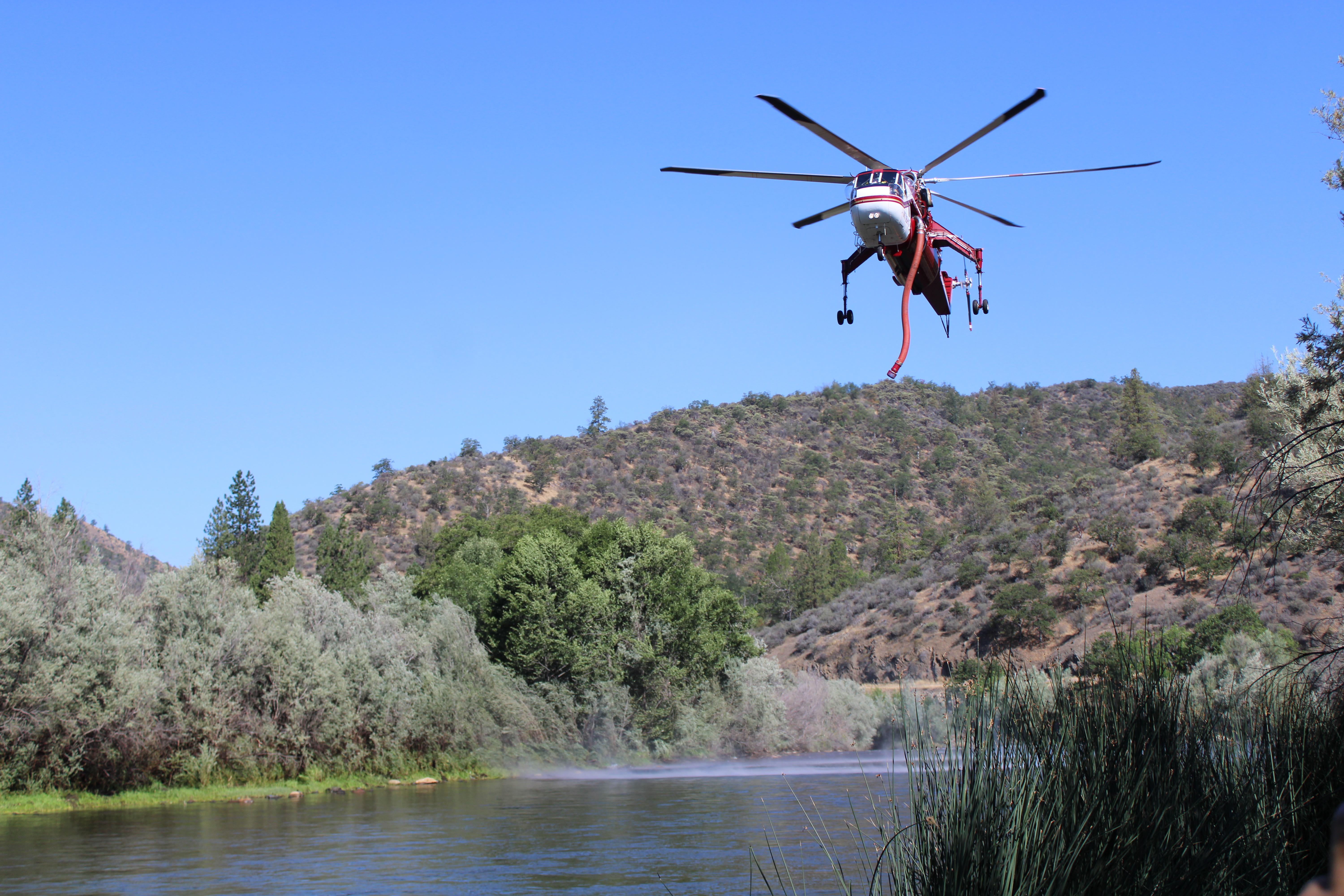 Helicopter transport Service helicopter 6HT dipping snorkel in Klamath River to fill with water 