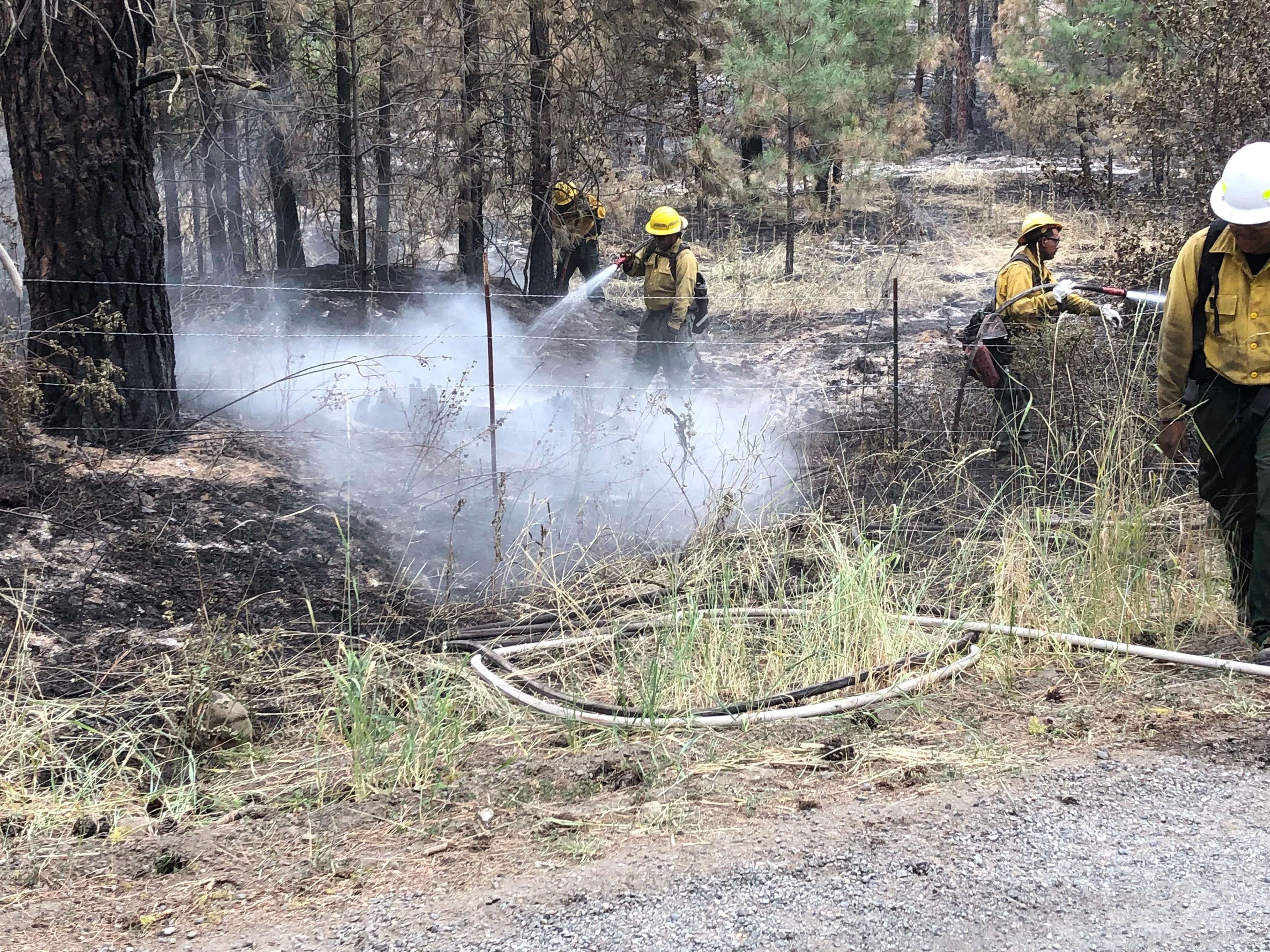 Firefighters are mopping up spraying water from a hose and mixing the water with dirt to fully extinguish the embers.