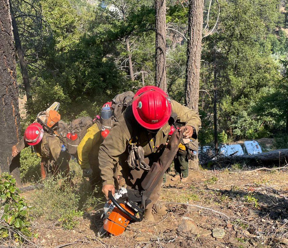 FIrefighters hike up hillside with their tools, leading with their sawyer and their chainsaw, up steep Klamath National Forest terrain.